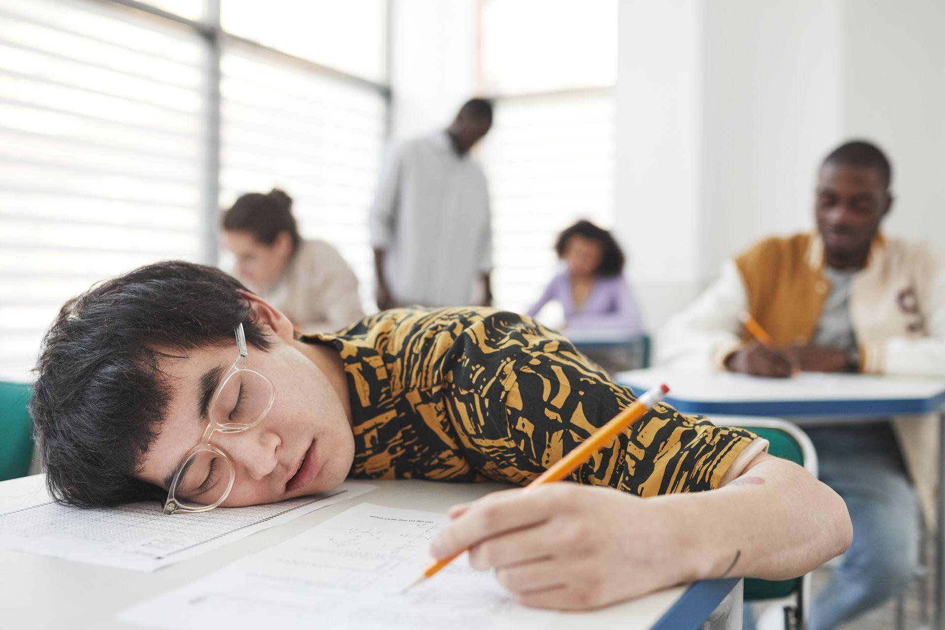 student falling asleep at their desk while writing in school