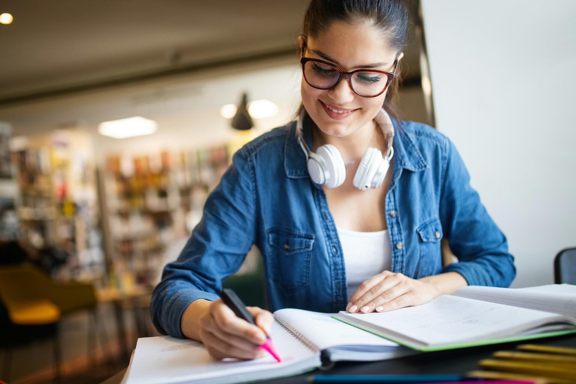 student writing notes in a notebook while referencing a textbook