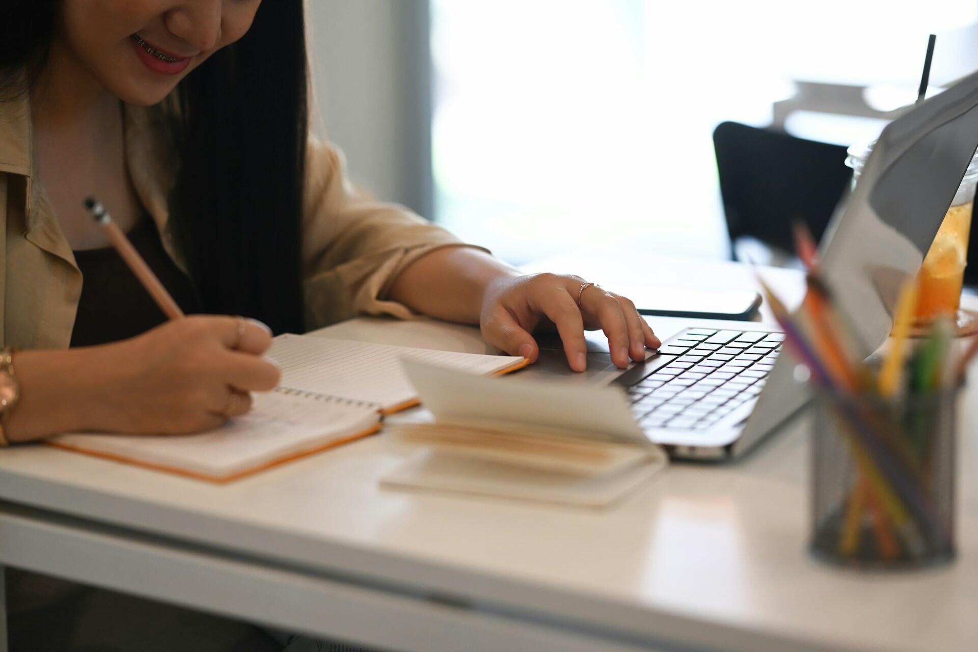 student with a laptop and writing in a a notebook in a quiet room