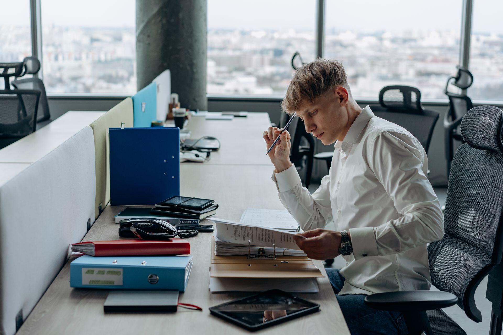young adult sitting at a desk with any folders, notebooks, and papers, including a tablet, reading and taking notes