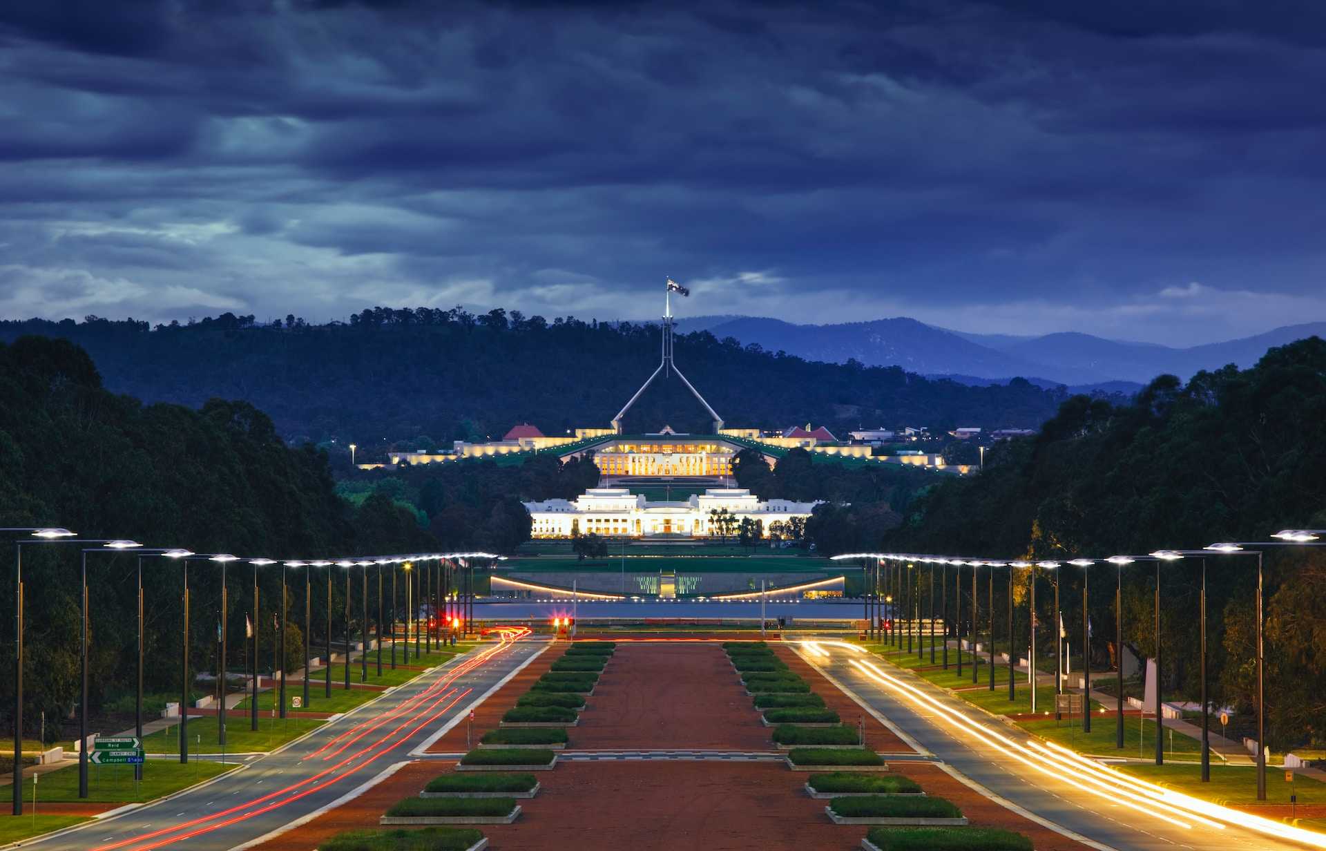 A panoramic view of the Australian Parliament lit up at dusk with its approach resembling an airport runway.