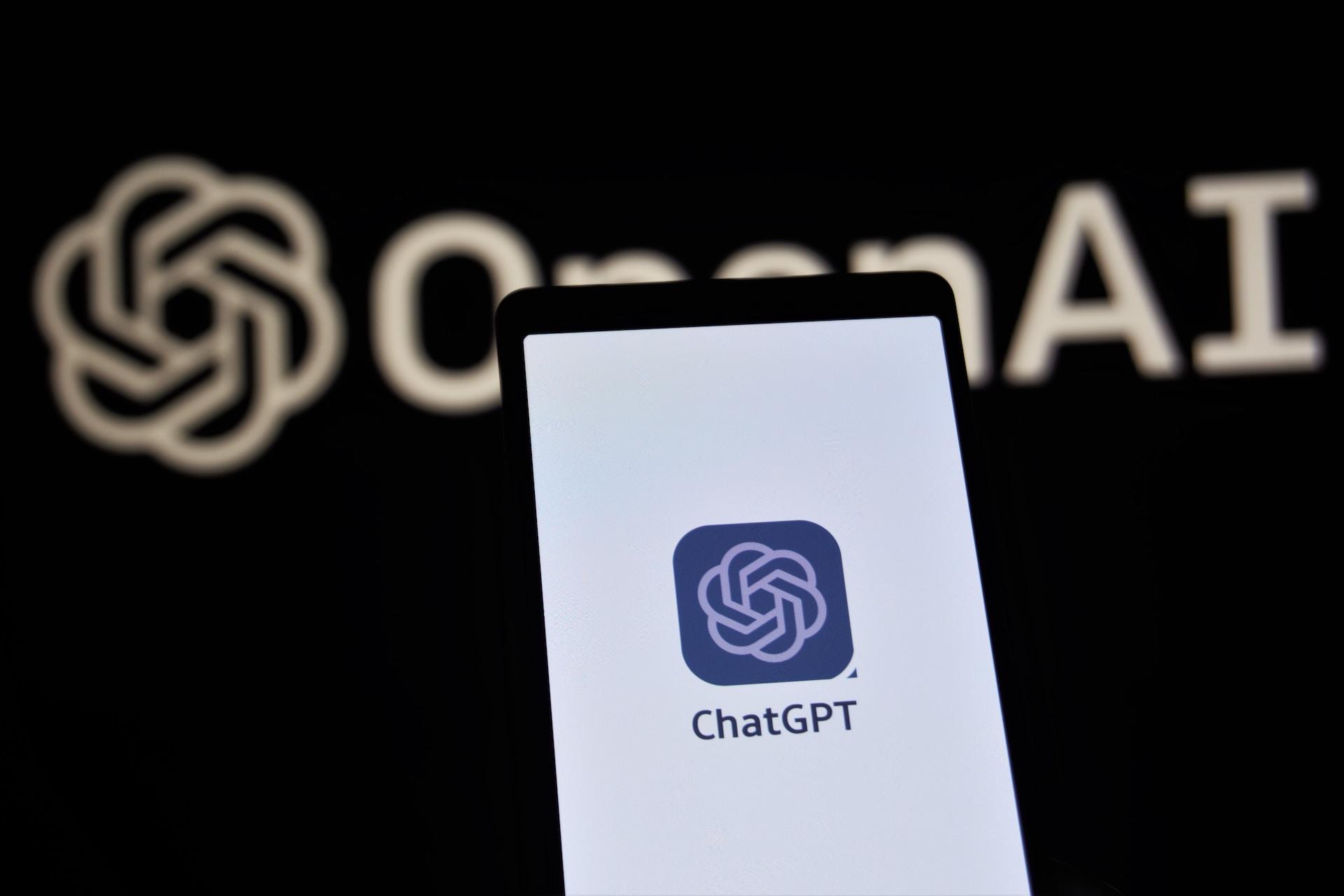 A phone with ChatGPT on the screen in front of a background reading OpenAI.