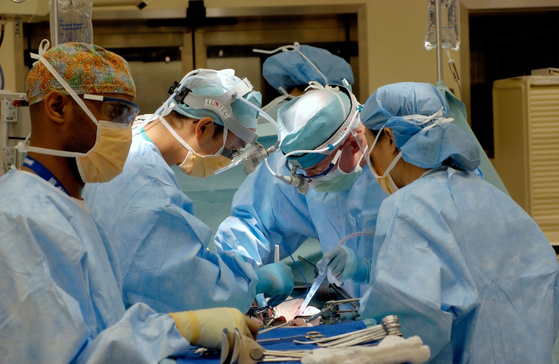 A group of people clad in surgical gear and wearing facemasks encircle an operating table to witness a procedure.