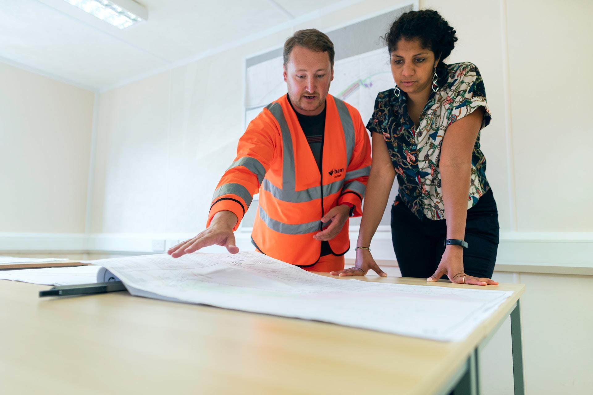 Two engineers looking at technical drawings on a table.