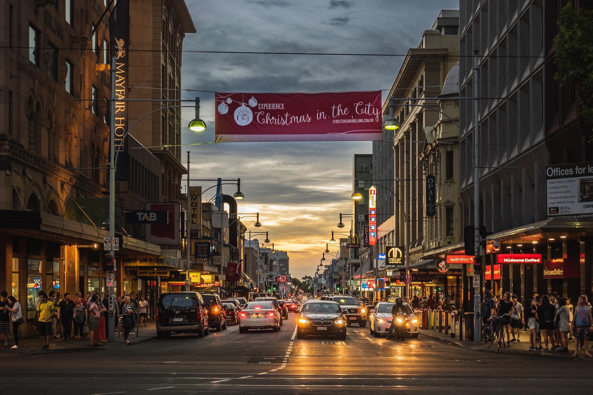 Rundle Mall seen at sunset, with the sidewalks crowded and a wine-coloured banner spanning the road