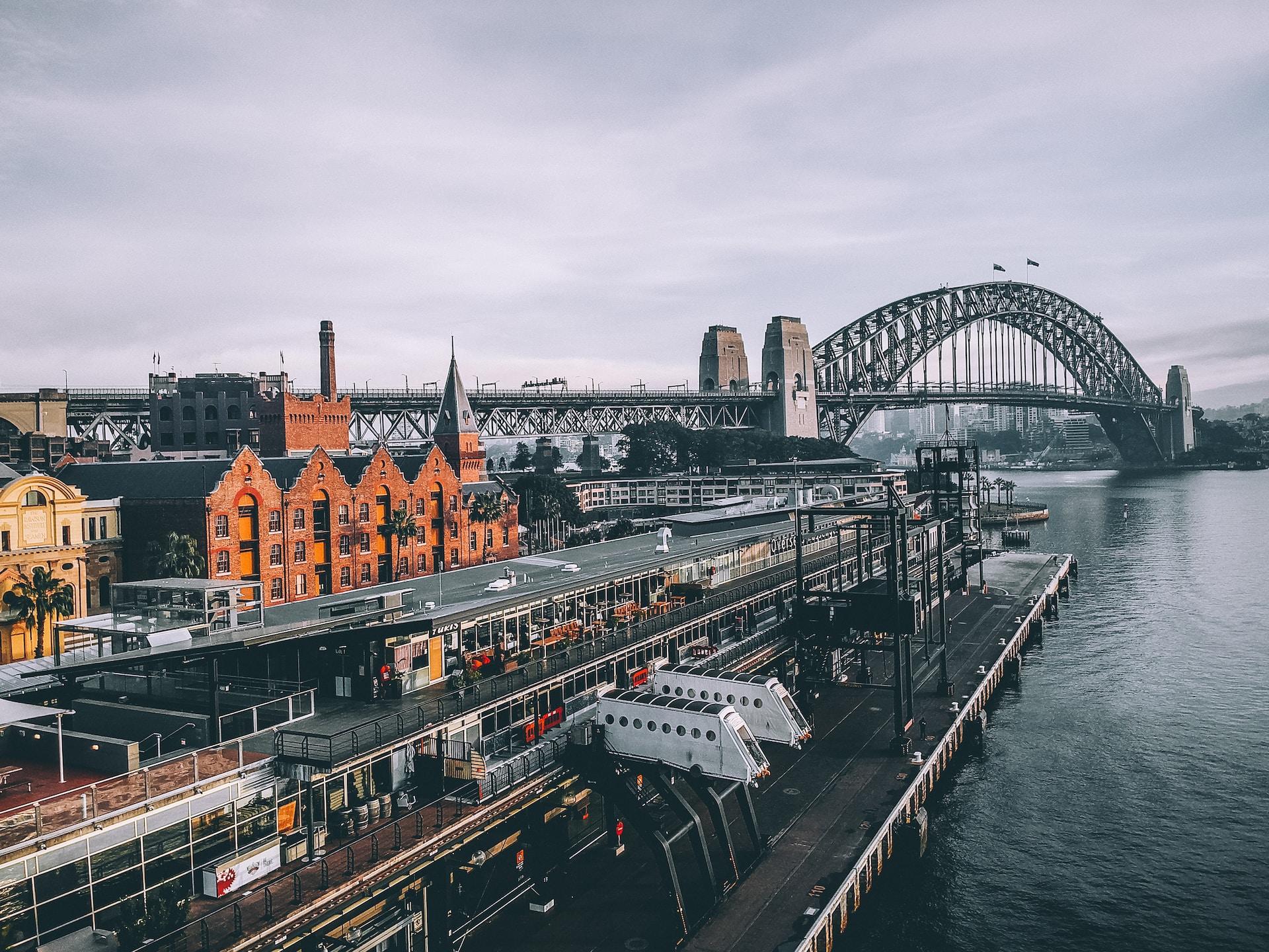 A panoramic view of the Sydney Bridge with the brick buildings to the left of the frame.