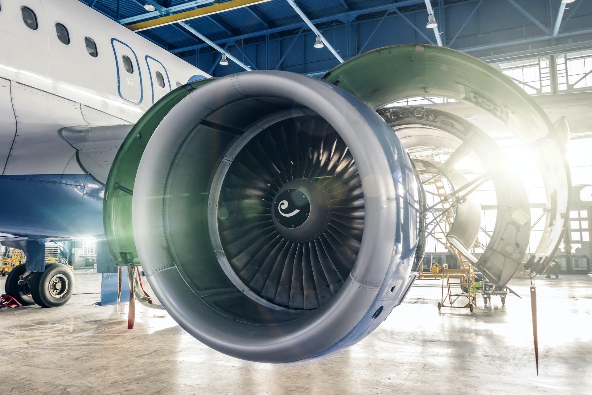 An airplane's engine affixed under the plane's wing, with its access panels open, glows in the early morning light streaming into the hangar.