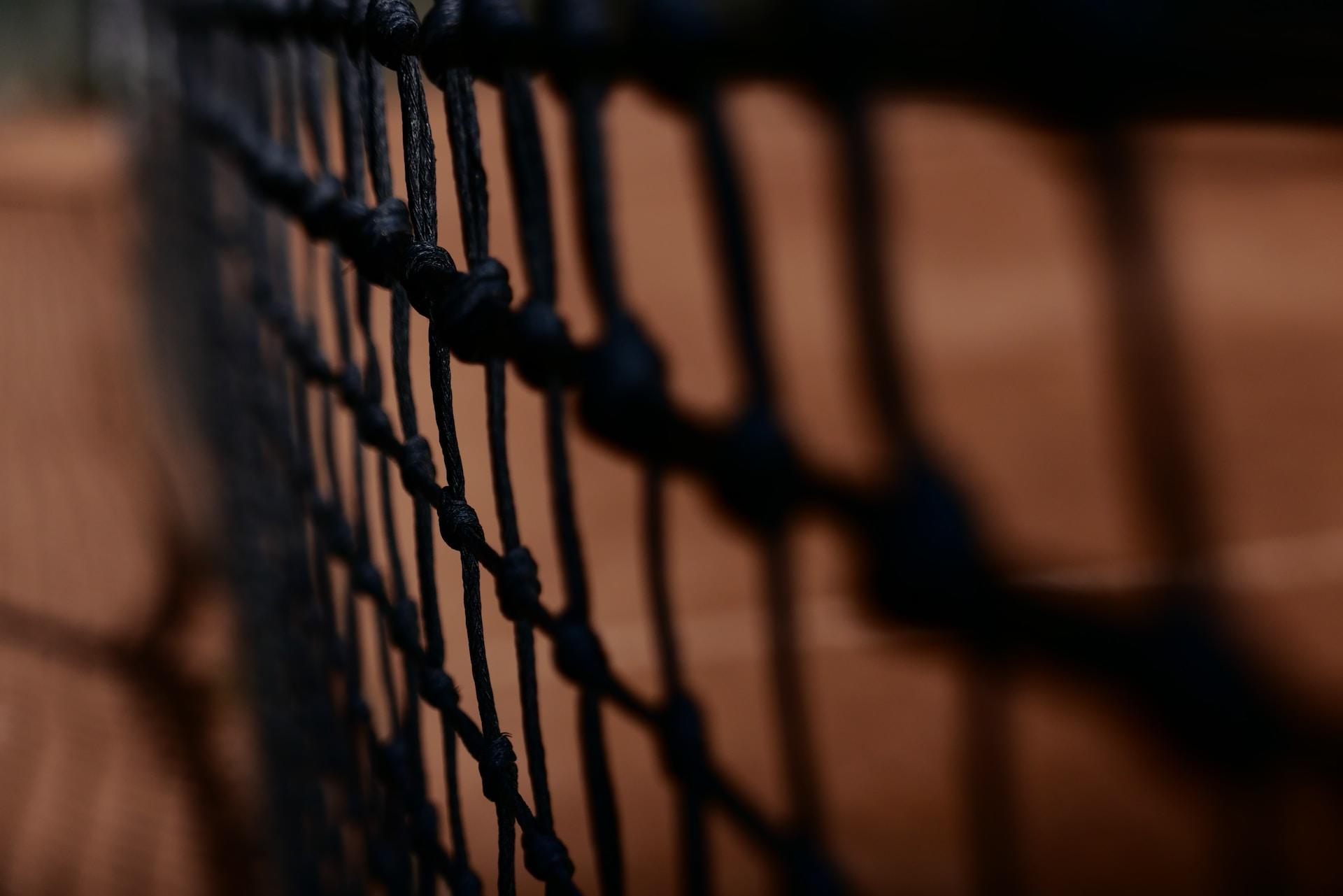 A closeup of a tennis net on a clay court.