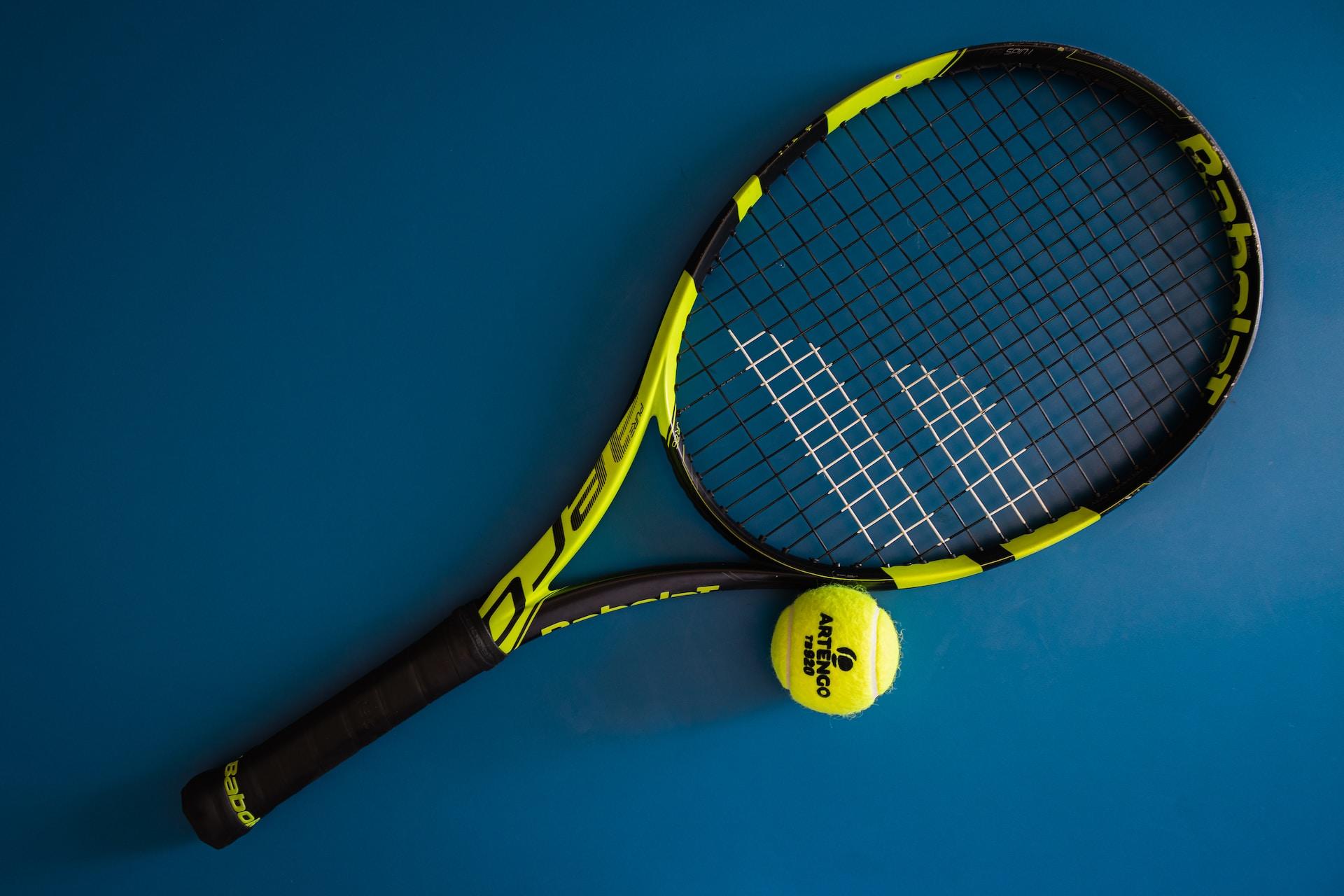 A tennis racket and a tennis ball on a hard court surface.