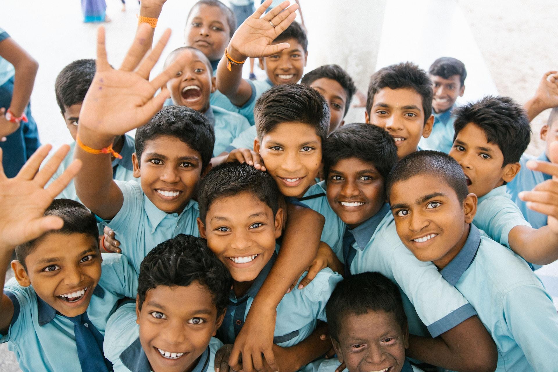 A group of boys wearing aqua coloured shirts with teal collars and ties bunch together smiling and waving at the camera.