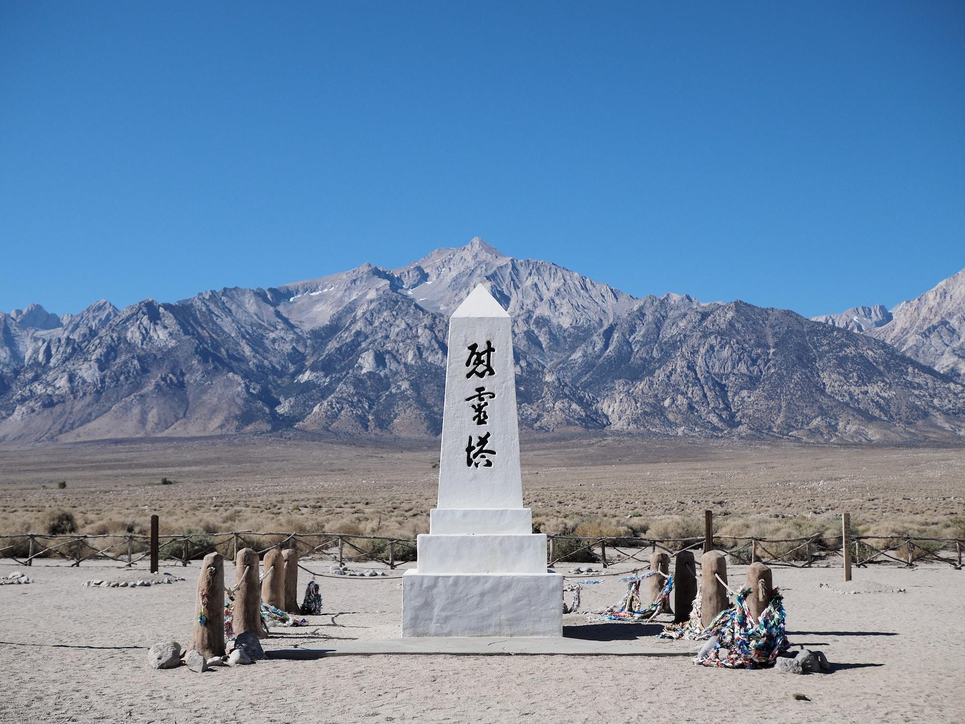 A white stone marker in California, ringed with eight short posts, set against a mountain range in commemorating the Japanese internment camps.