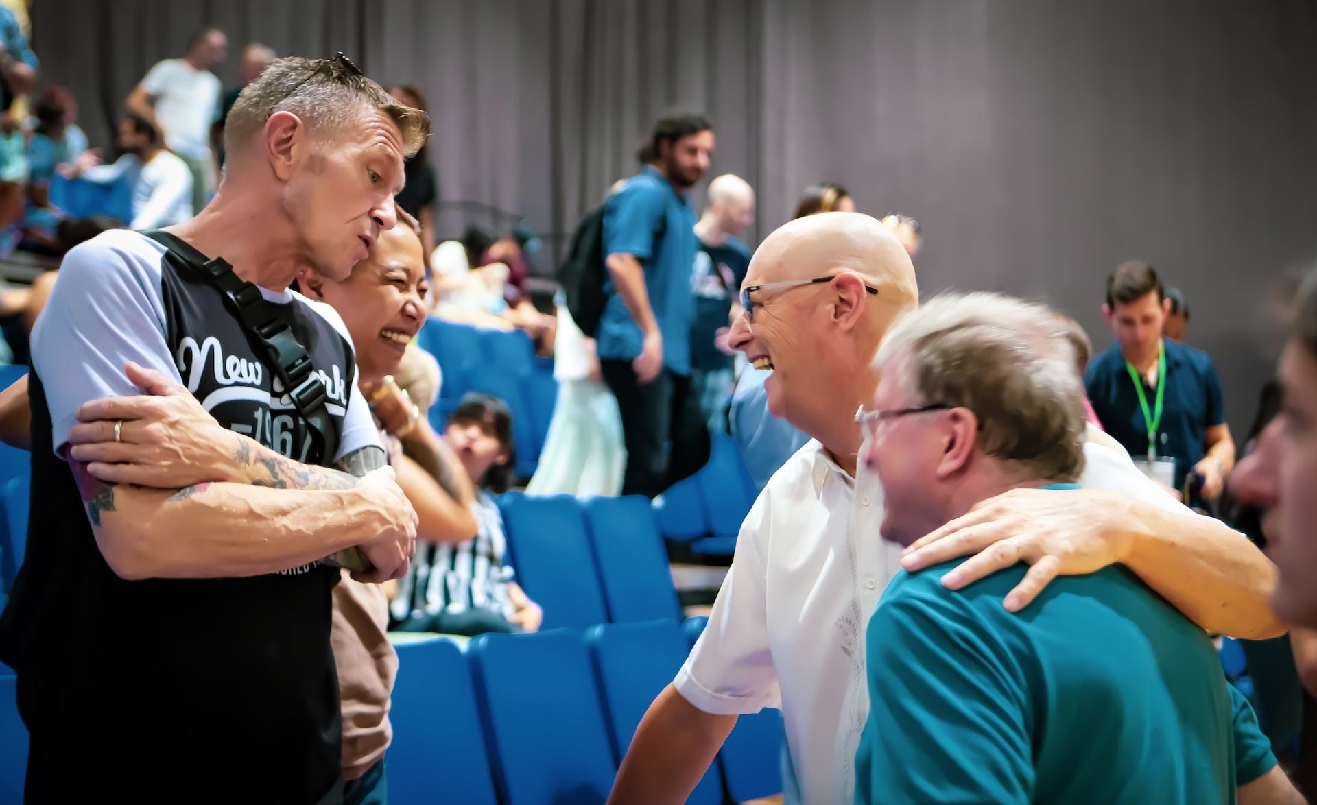 A group of men stand in an auditorium with blue seats, smiling and talking together.