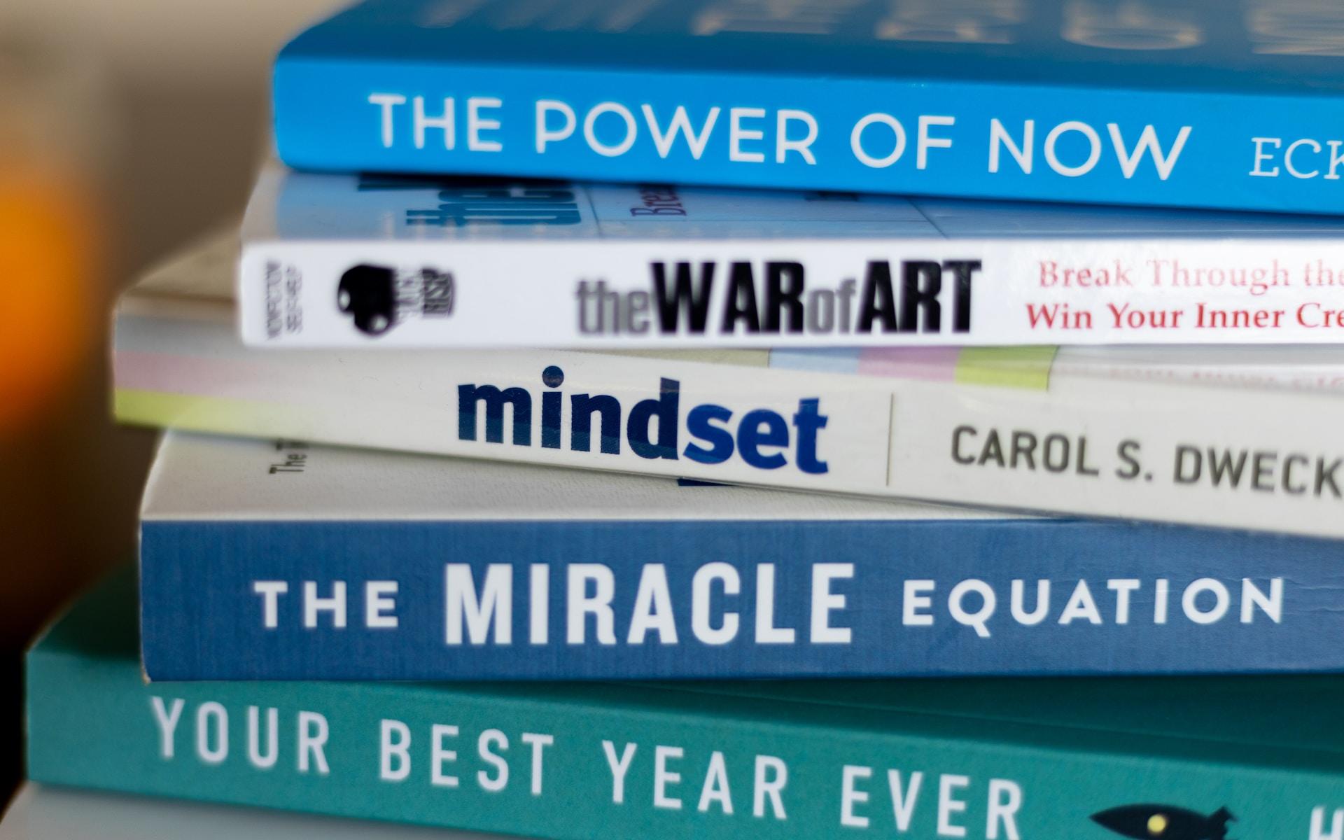 A pile of books laid on their covers with the spines showing, with the titles indicating self-help themes.