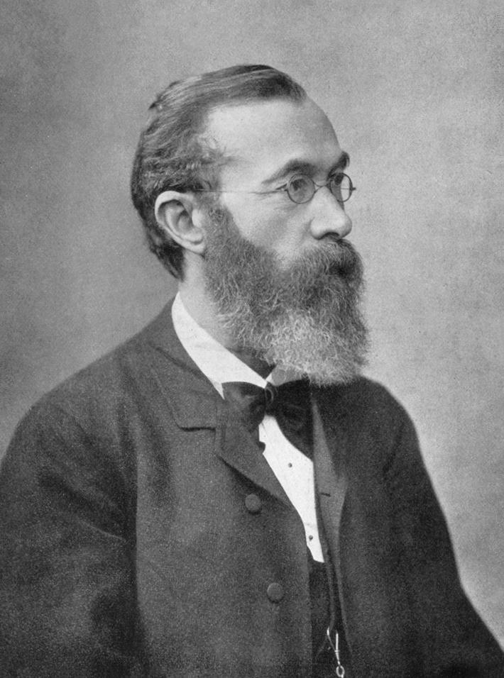 A greyscale portrait of Dr Wilhelm Wundt, taken in 1902. He wears round wire-framed spectacles and a bowtie with a three-piece suit. He faces right and has an ample beard and mustache.
