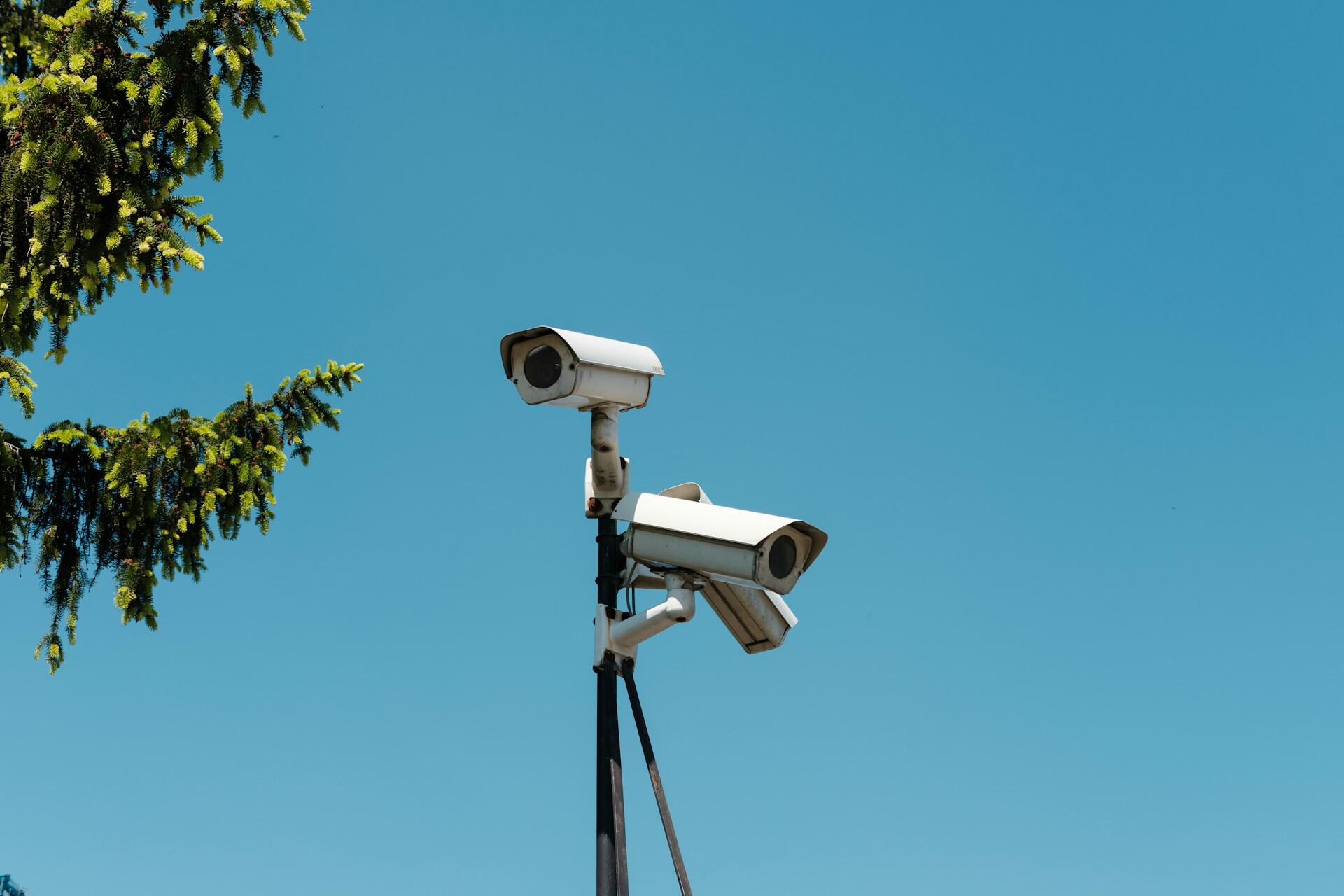 Two security cameras mounted on a pole against a blue sky