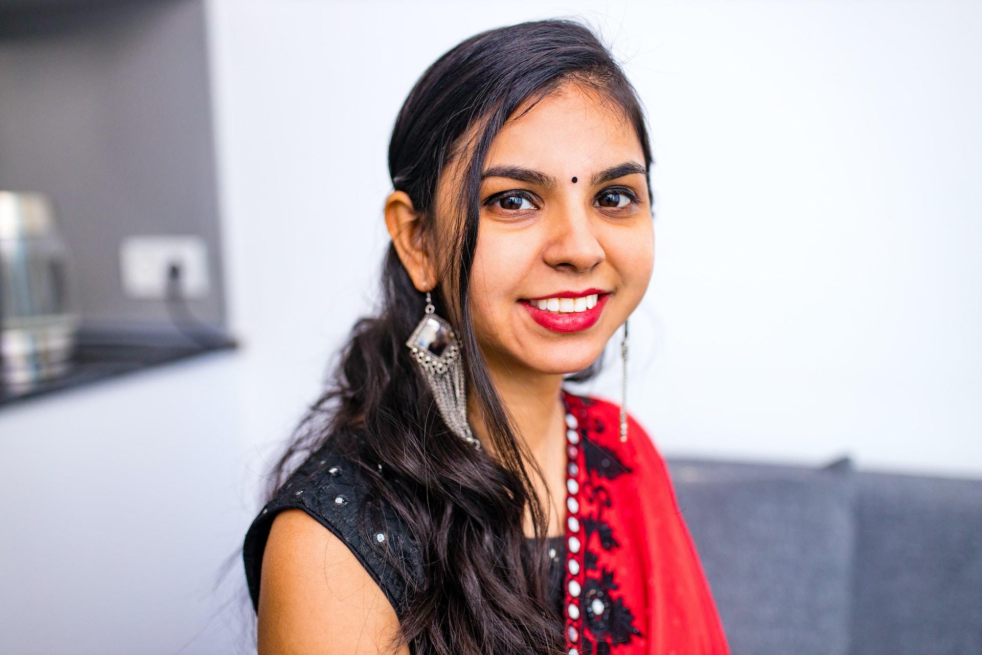 A woman wears a black and red sari, her hair combed back and smiling at the camera.