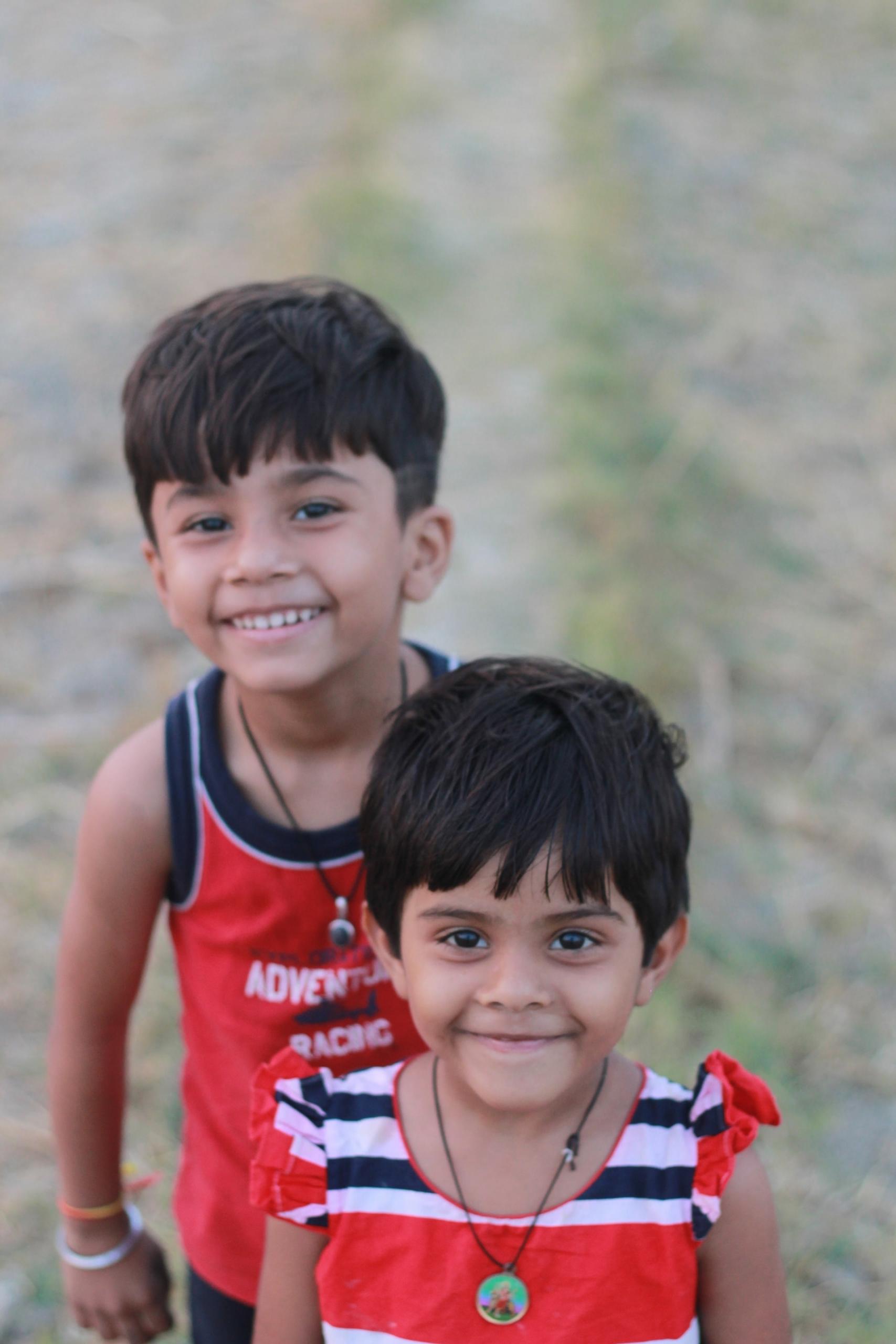 Two young children, both dressed in bright red clothing with blue and white accents, pose and smile at the camera.