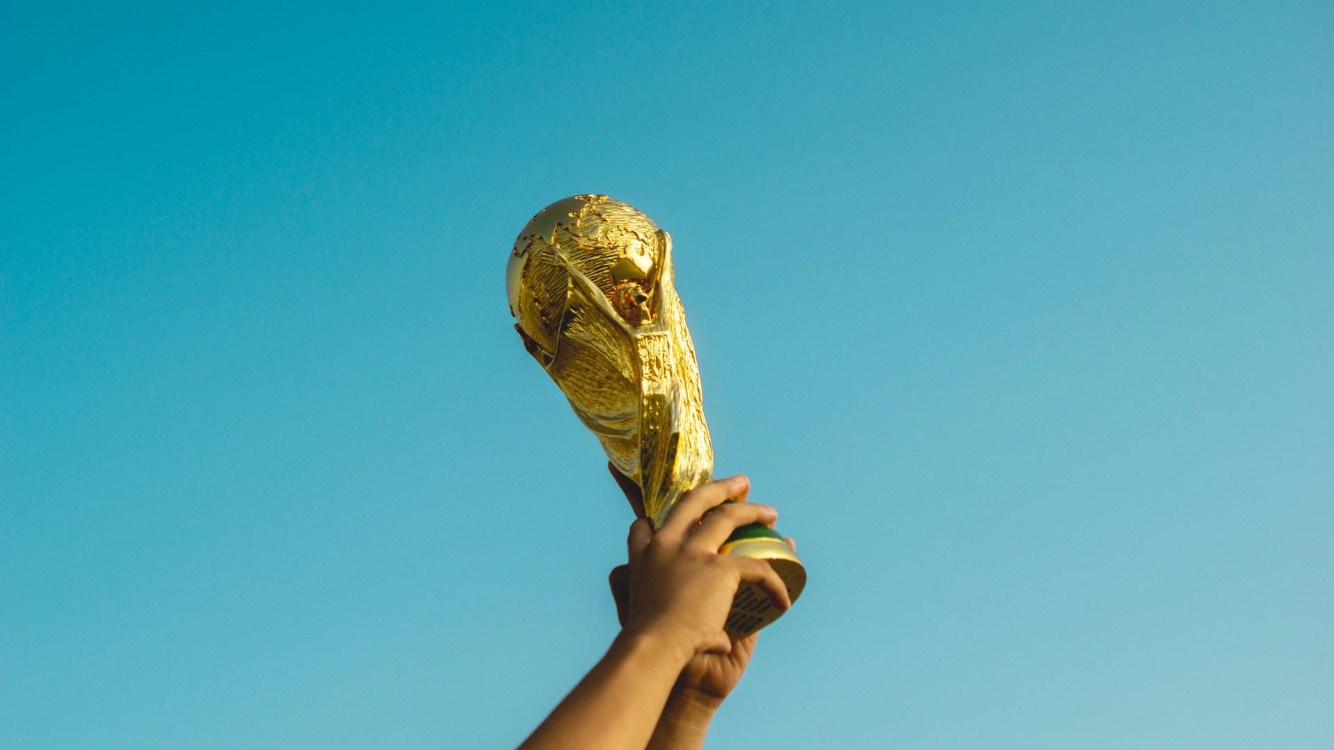 A person holds aloft a Ballon D'or trophy against a bright blue sky, which makes the award appear more golden.