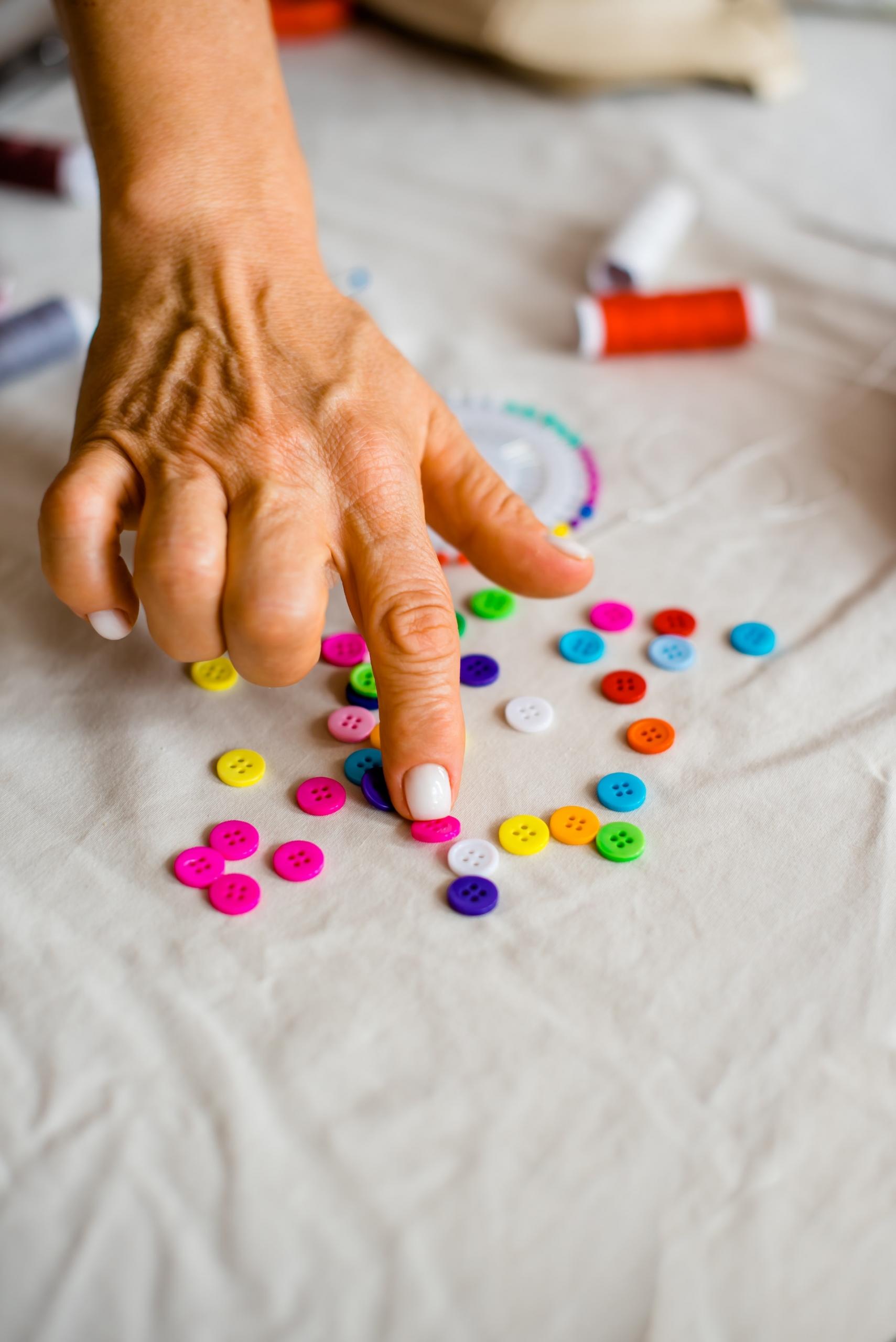 A person's hand points to a scattering of bright, colourful buttons scattered on a white piece of cloth.