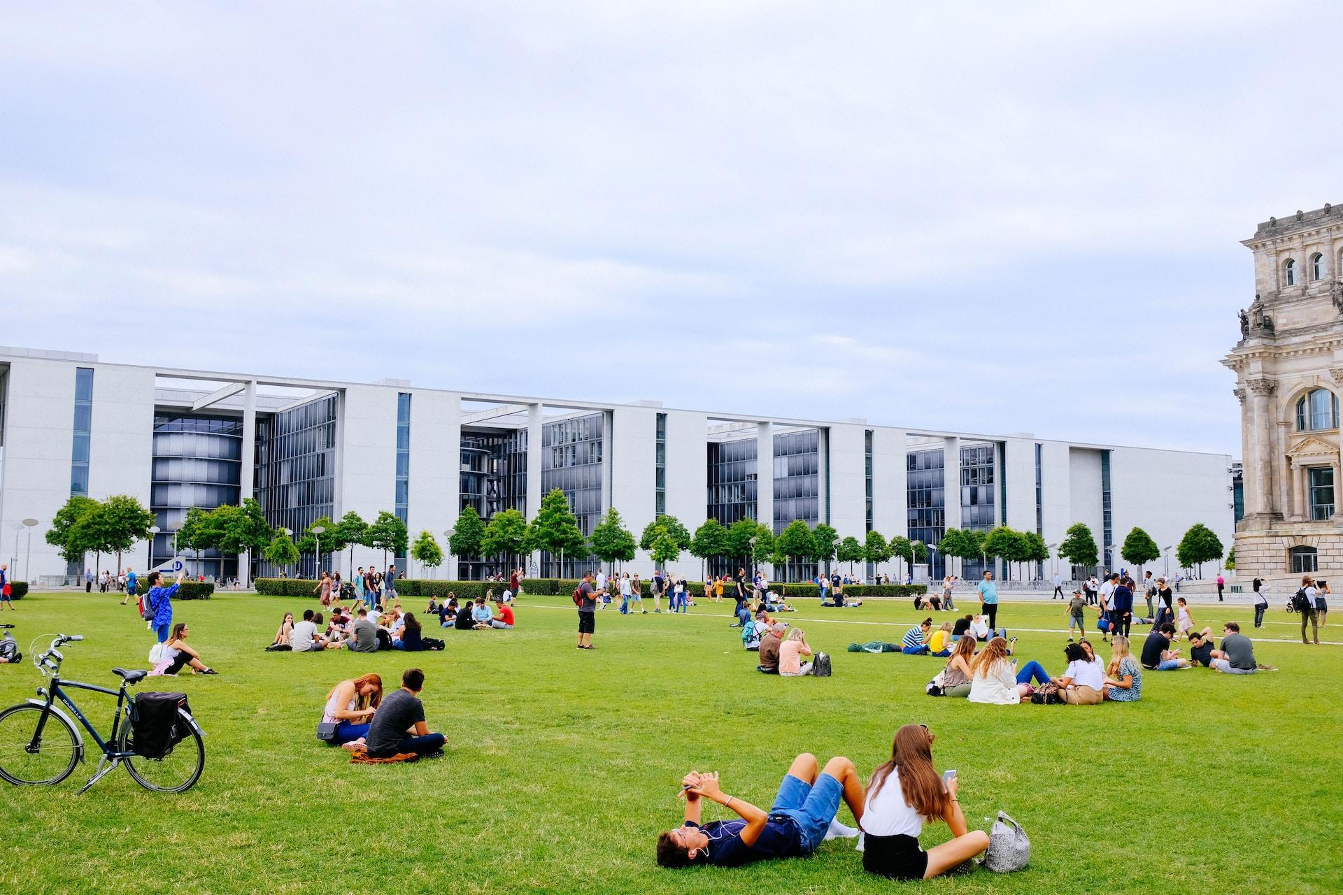 A warm day with light clouds invites students to loll on their school campus green with the white modern building forming the backdrop. 