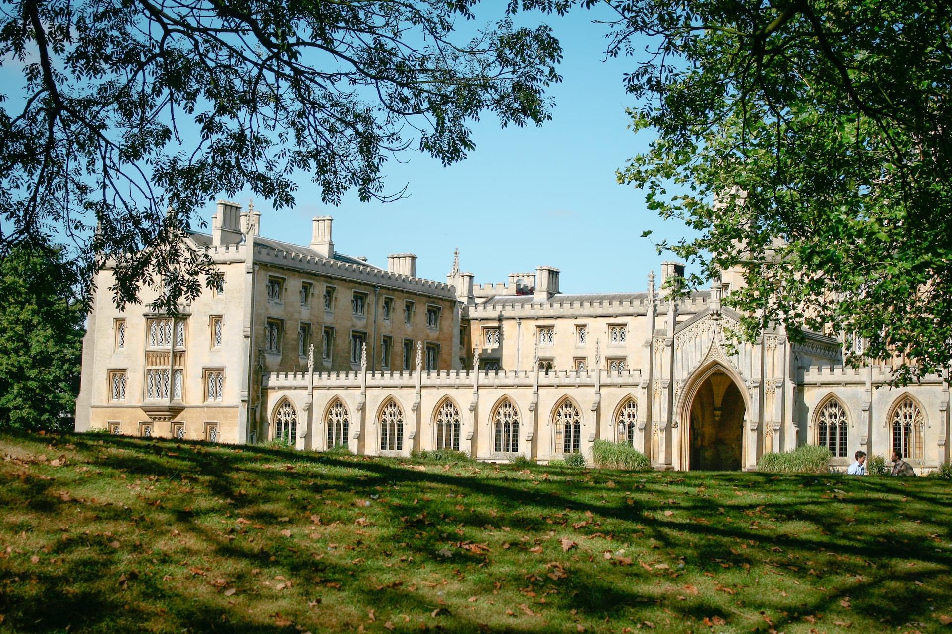 A regal looking building in light coloured stone seen from across a green space on a sunny day. 
