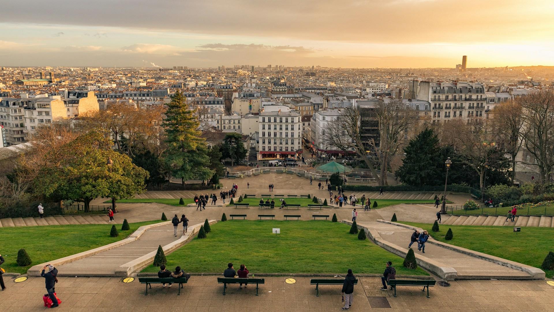 Overlooking Paris from a hilltop at sunset, with people strolling and sitting on benches.