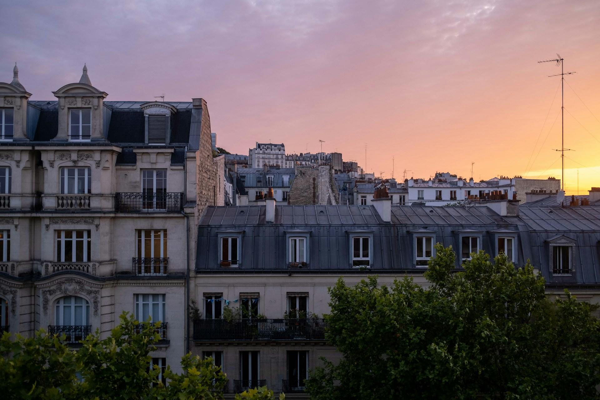 Parisian rooftops at sunset with a warm sky.