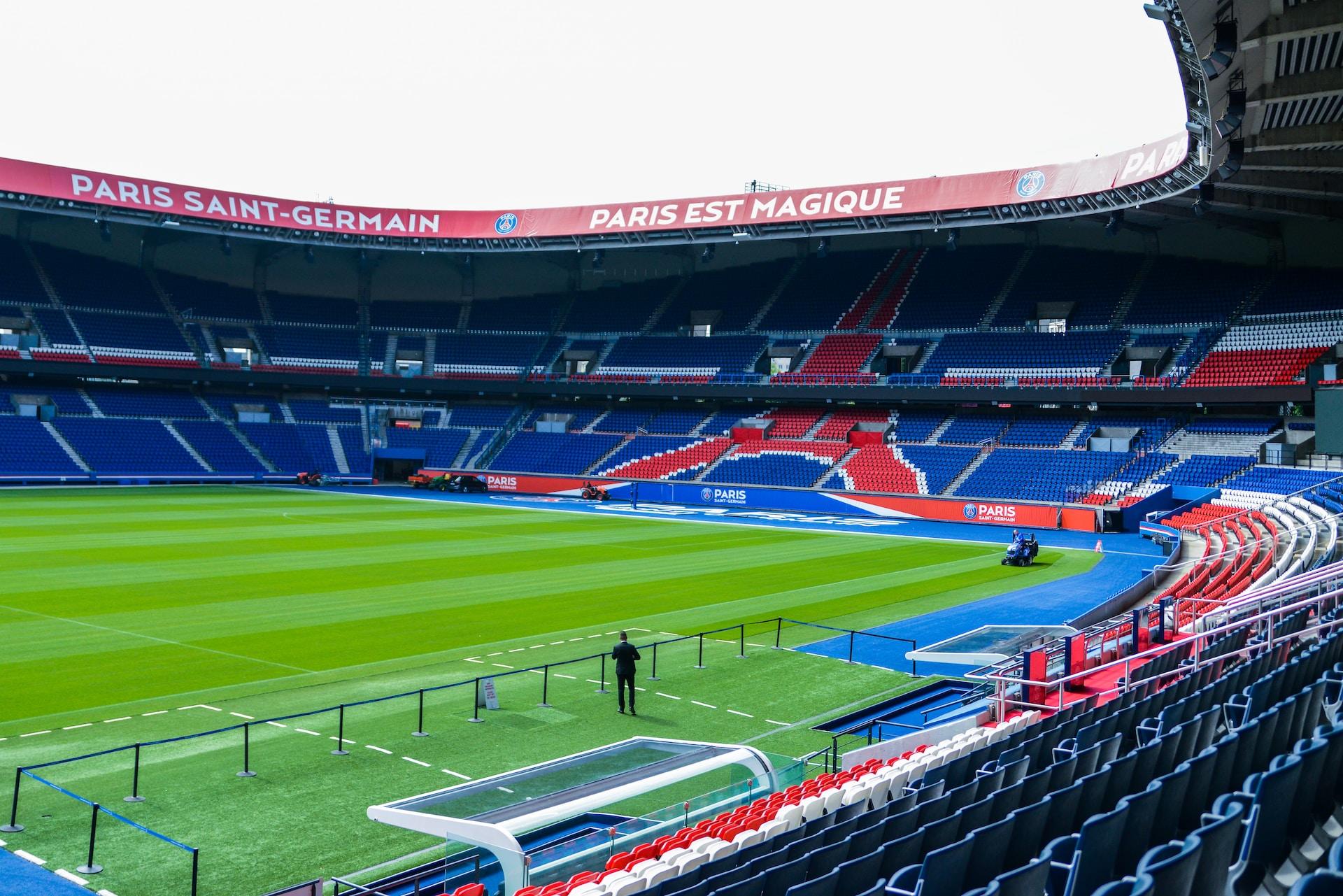 The empty Paris Saint-Germain soccer stadium, with its bright green pitch contrasting with the red and blue stands. 