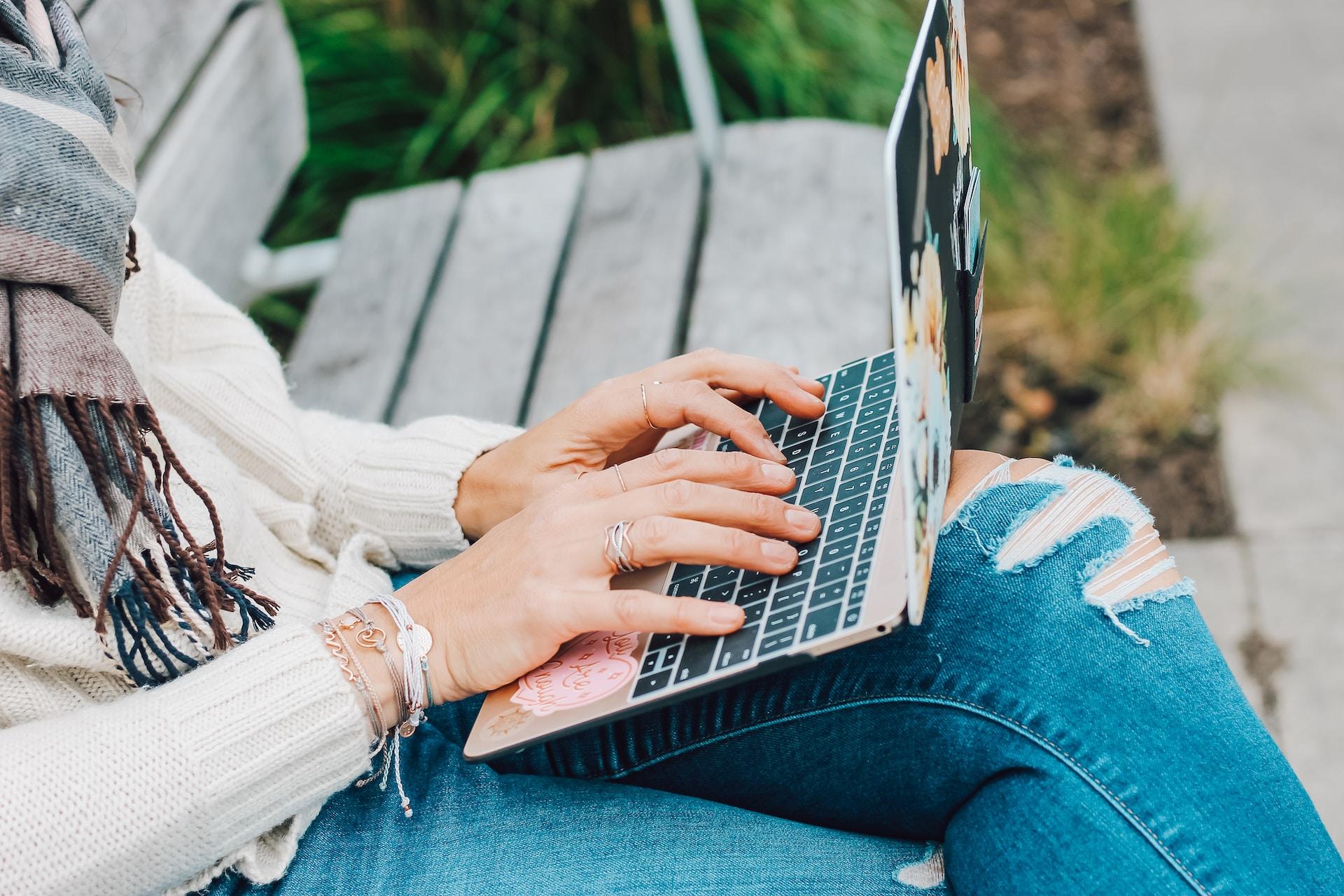 A person sitting on a park bench typing on a laptop.