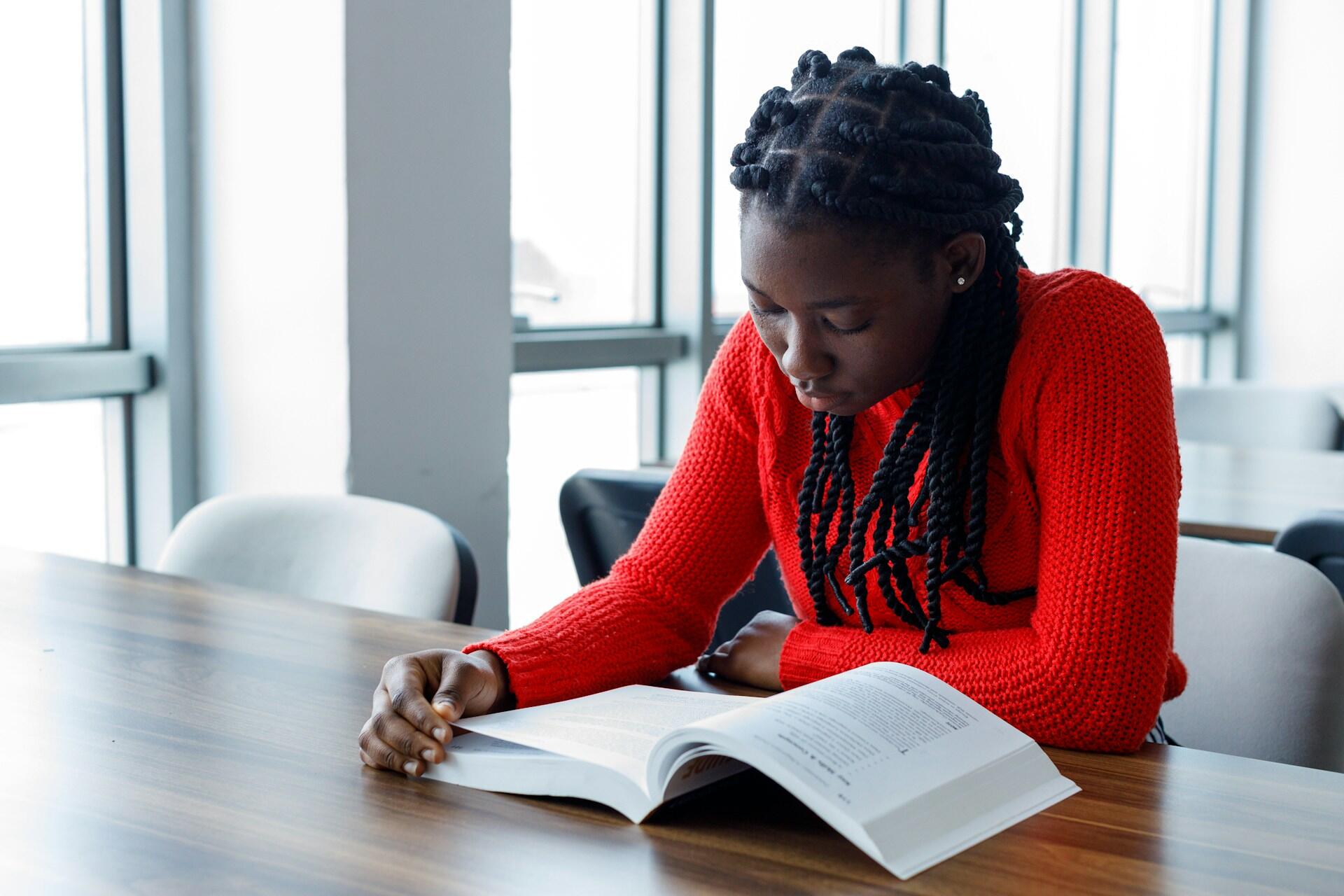 A person in a red shirt reads a book at a table.