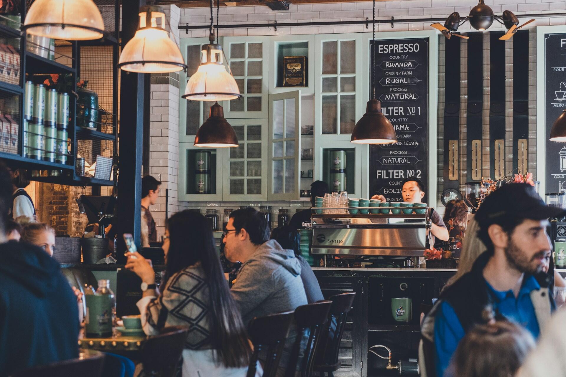 people sitting inside a café with a counter, coffee machine, and hanging lights
