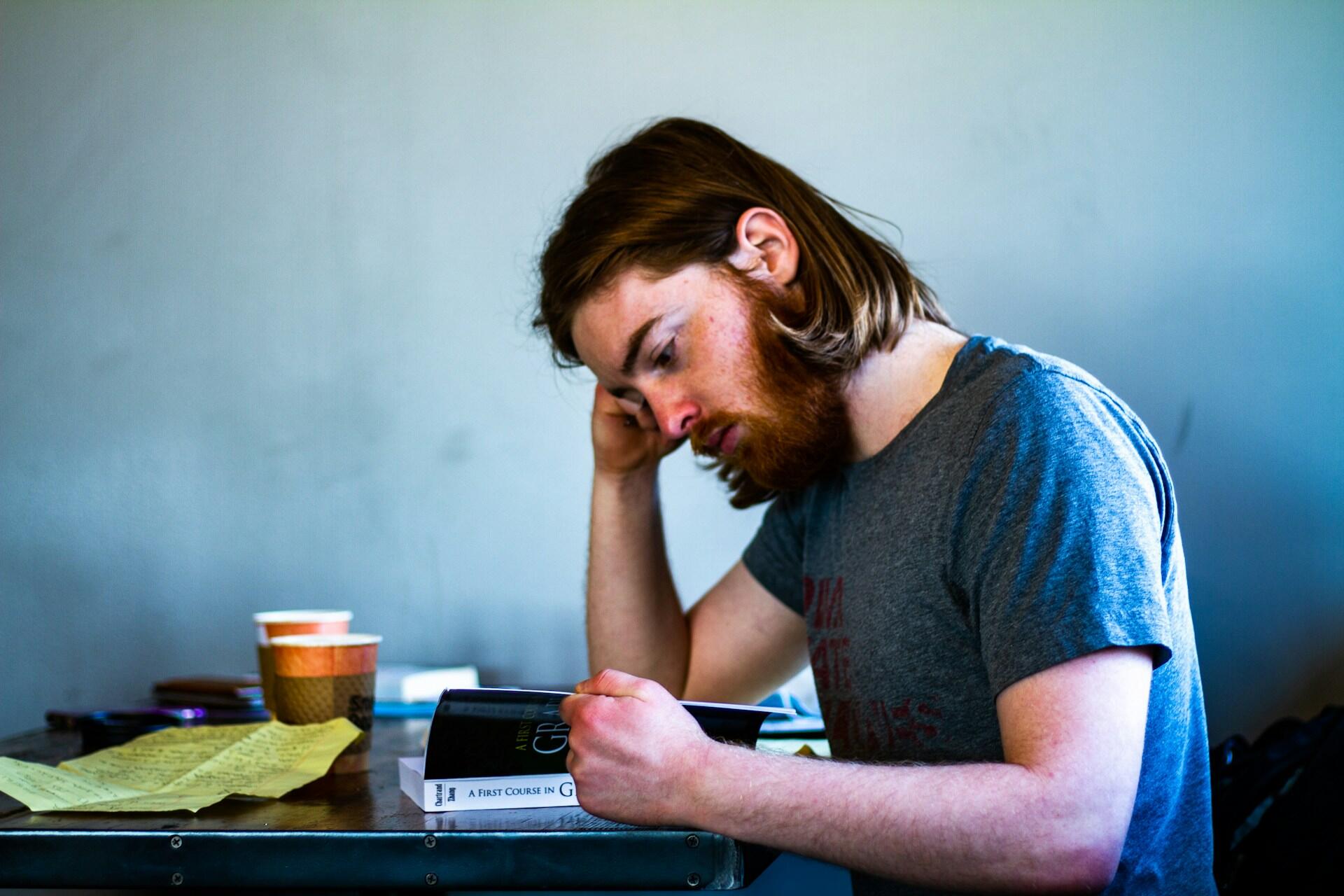 man reading a book at a table with notes and a coffee cup
