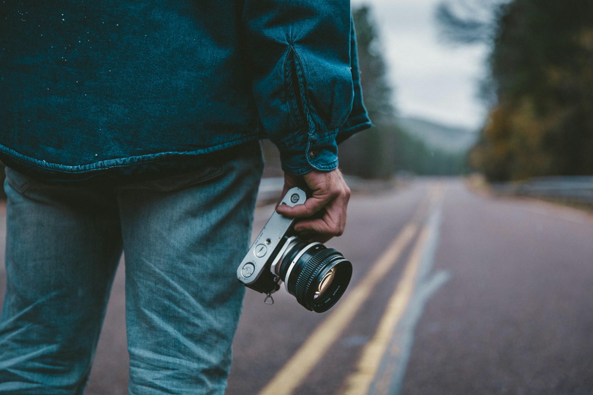 A person holding a camera on a road.