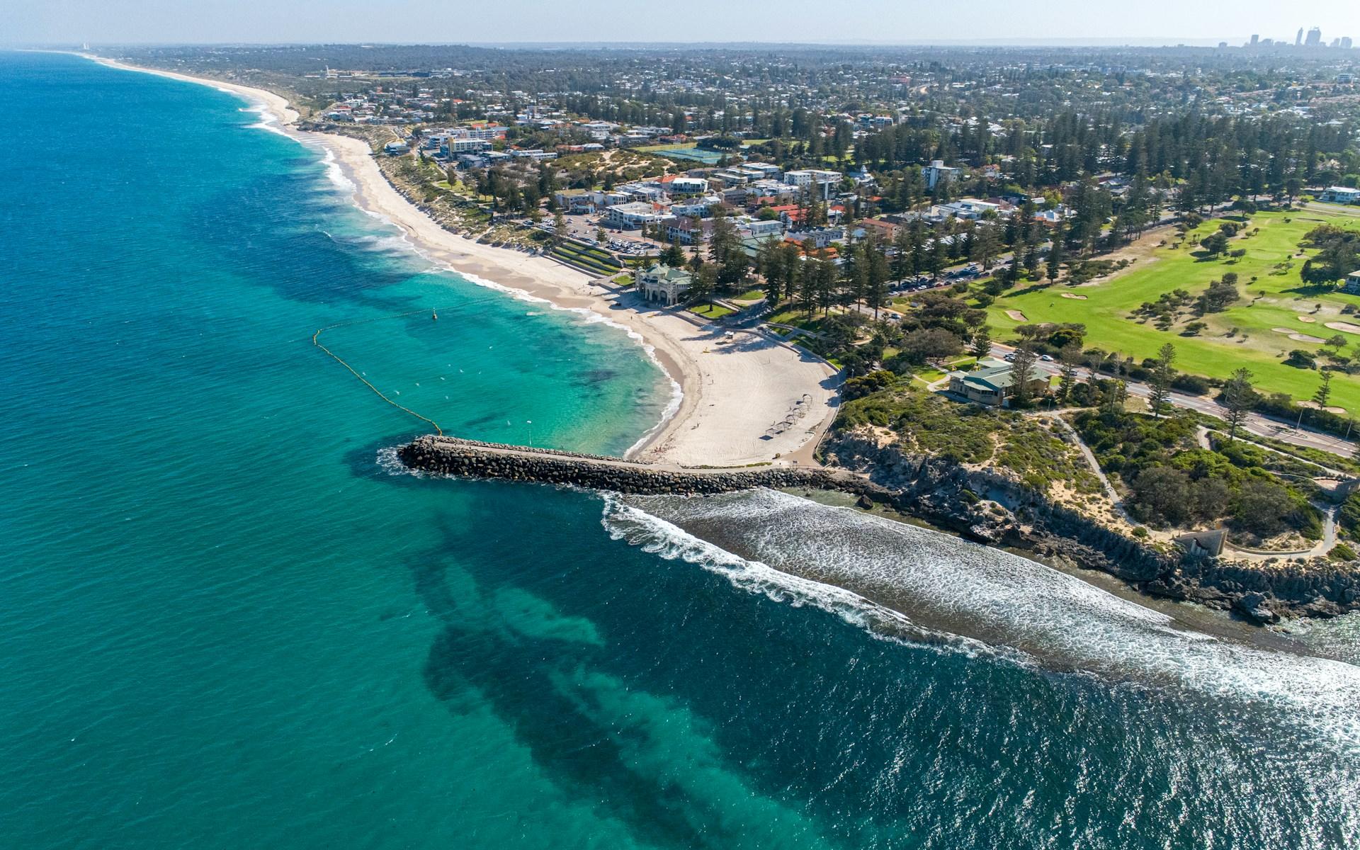 An aerial view of Cottesloe Beach which shows its clear waters and white sandy beach, as well as a pier that descends into the water.
