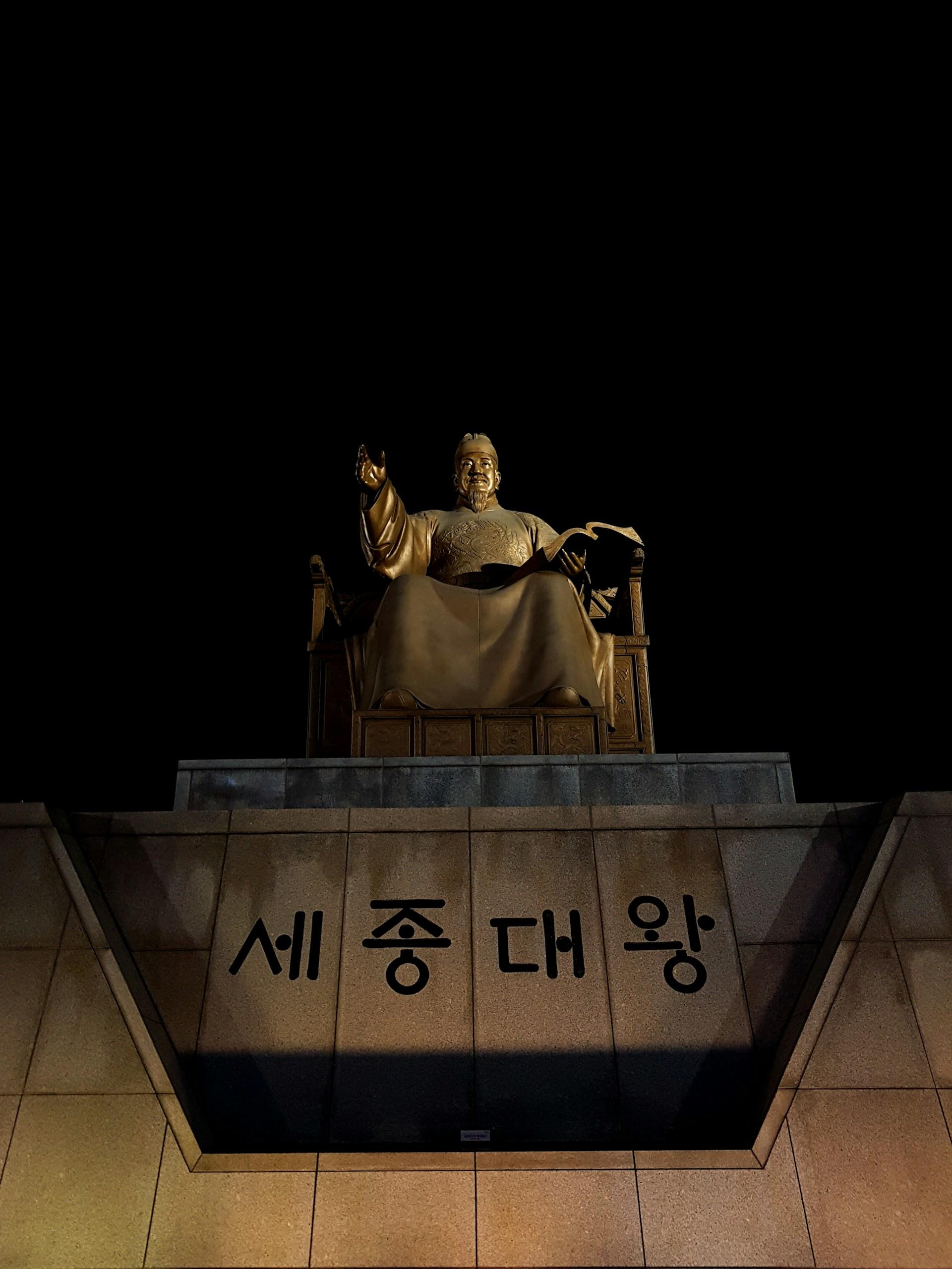The large bronze statue of Korean King Sejong the Great at Gwangwhamun Square in Seoul, seen at night, with 4 Korean characters on the statue's base.  