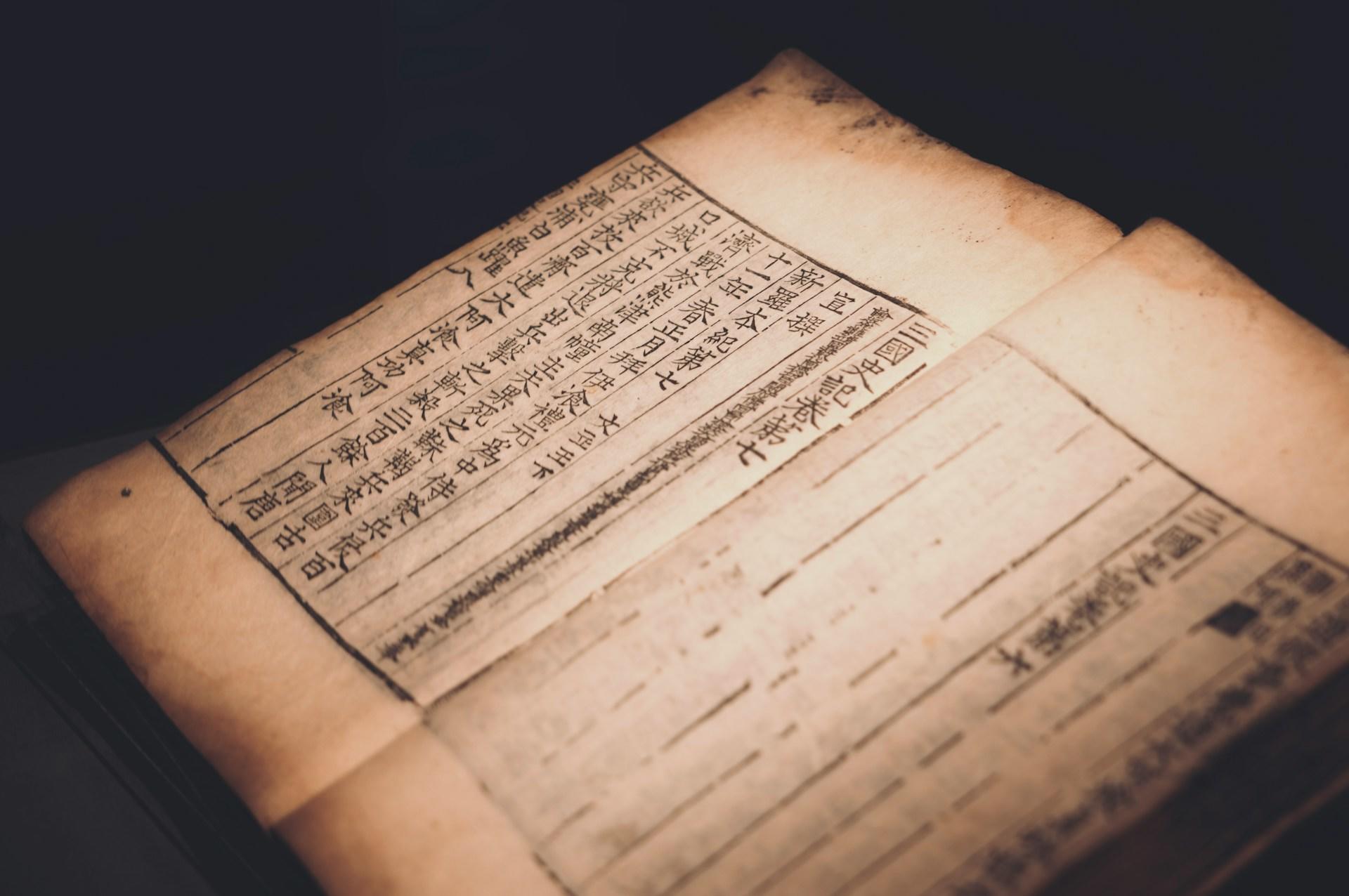 An ancient Korean manuscript open to reveal Mandarin columnar writing, penned in black ink against sepia-toned paper on a black background. 
