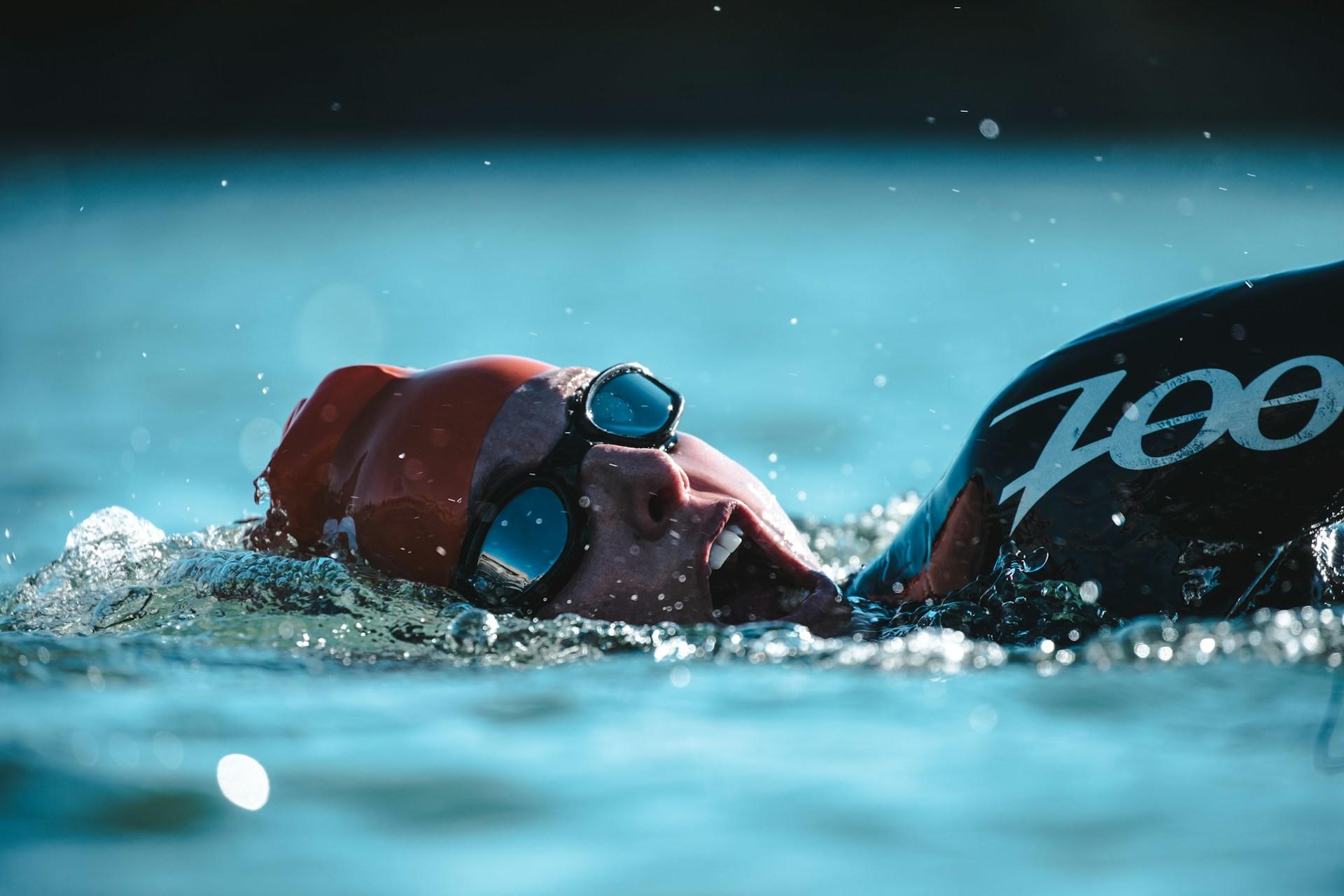 A man in a wetsuit and swim cap swimming.
