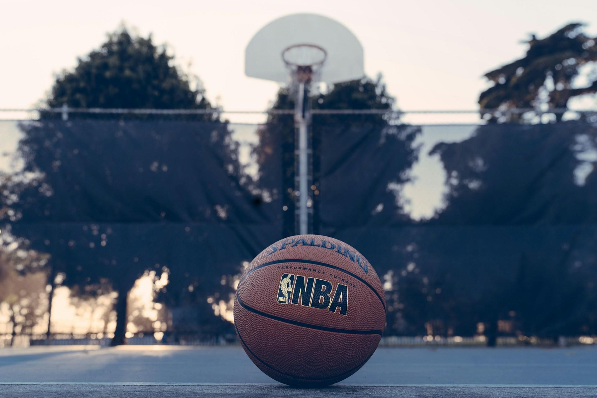An basketball with the NBA logo sitting on the ground of an outdoor court