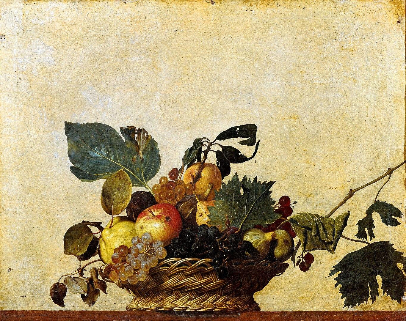 A basket of fruit with green leaves against a yellow wall.