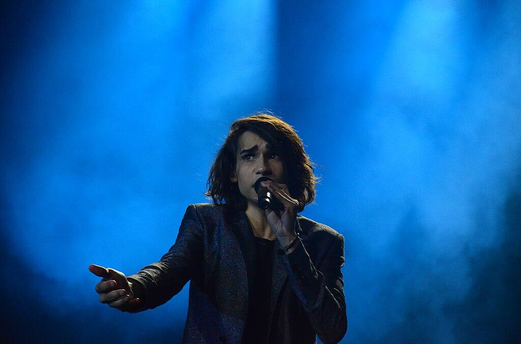 Isaiah Firebrace singing in front of a bright blue background