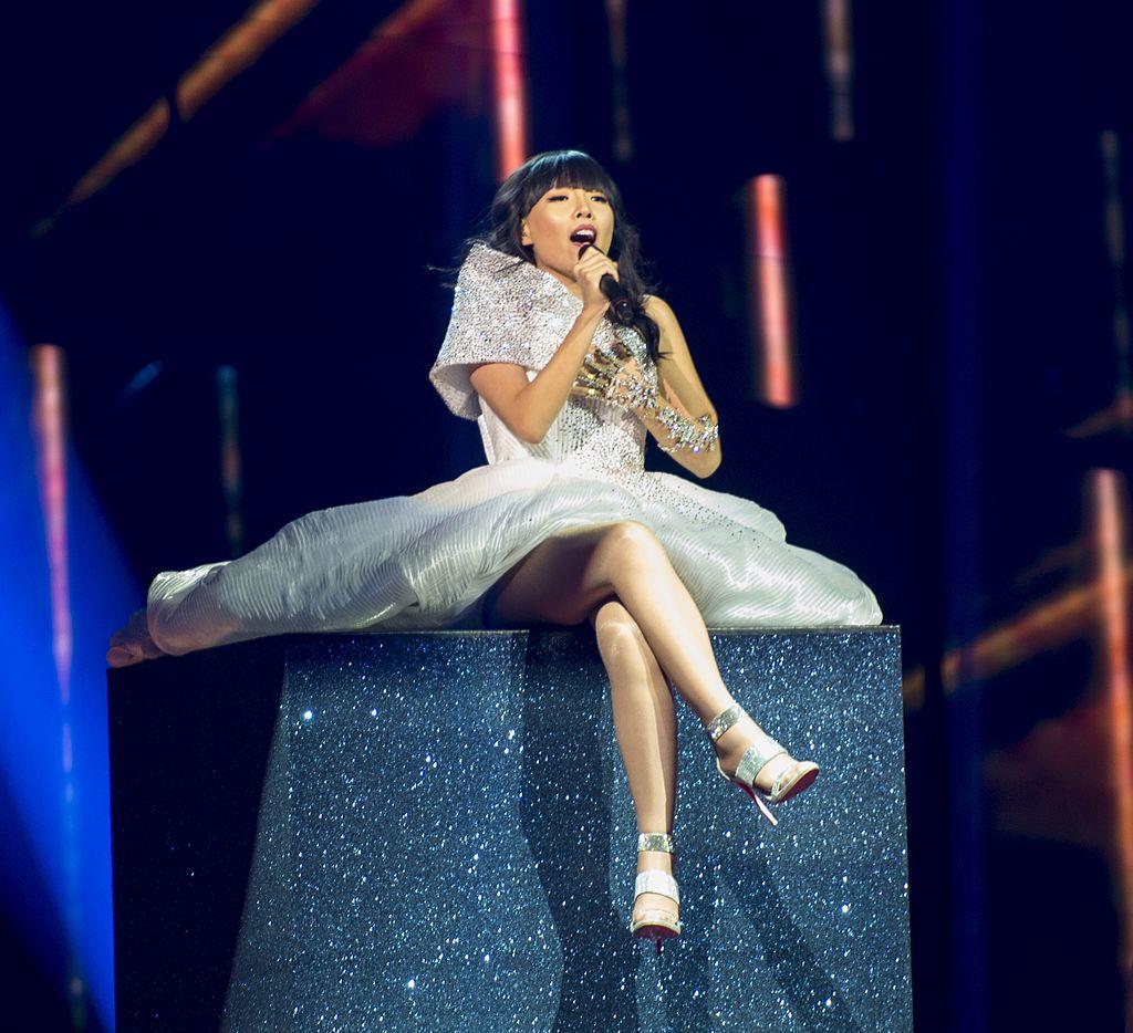 A woman in a white dress sitting on a box on stage and singing.