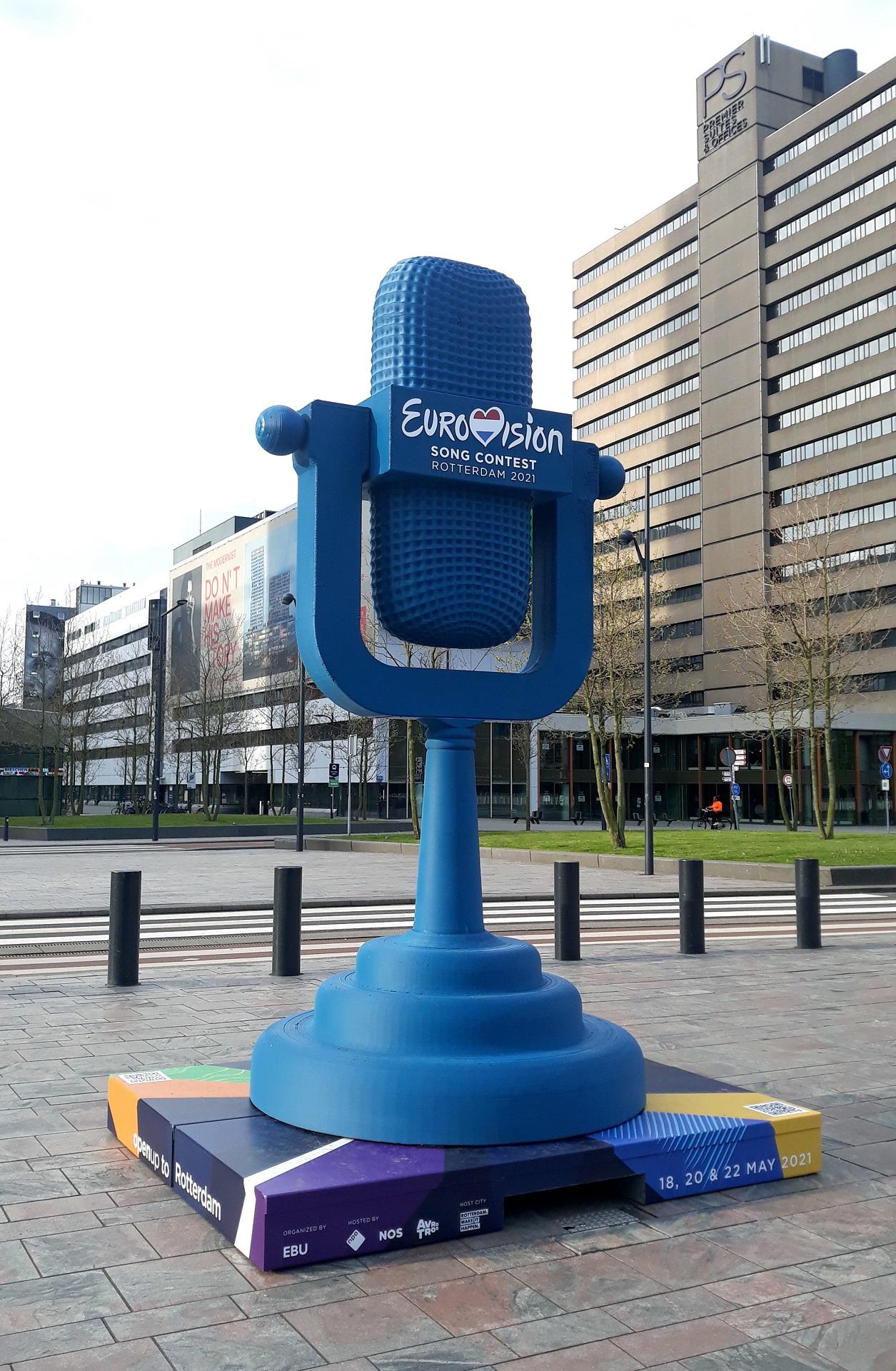 A replica of the Eurovision trophy, shaped like a microphone and coloured blue, with the word Eurovision Song Contest in white letters sits in a plaza in Rotterdam.