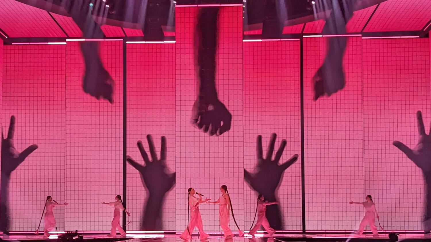 Vesna and dance performers on stage with a screen wall depicting large images of hands in the background