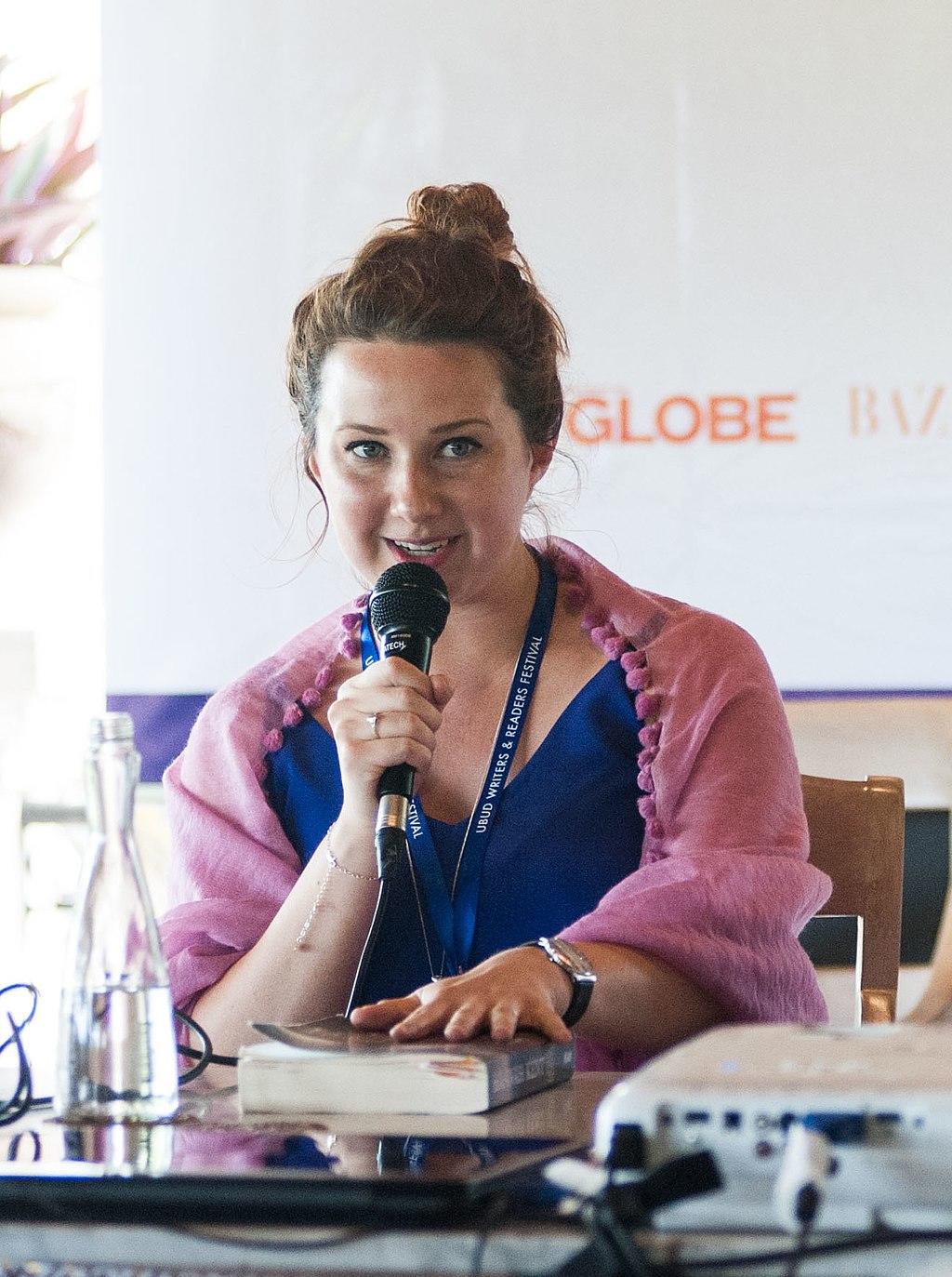 A woman sitting at a table with a microphone, speaking at a conference.