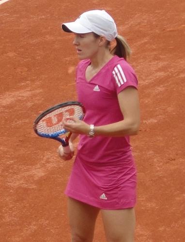 A female tennis player in a pink tennis outfit on a clay court.