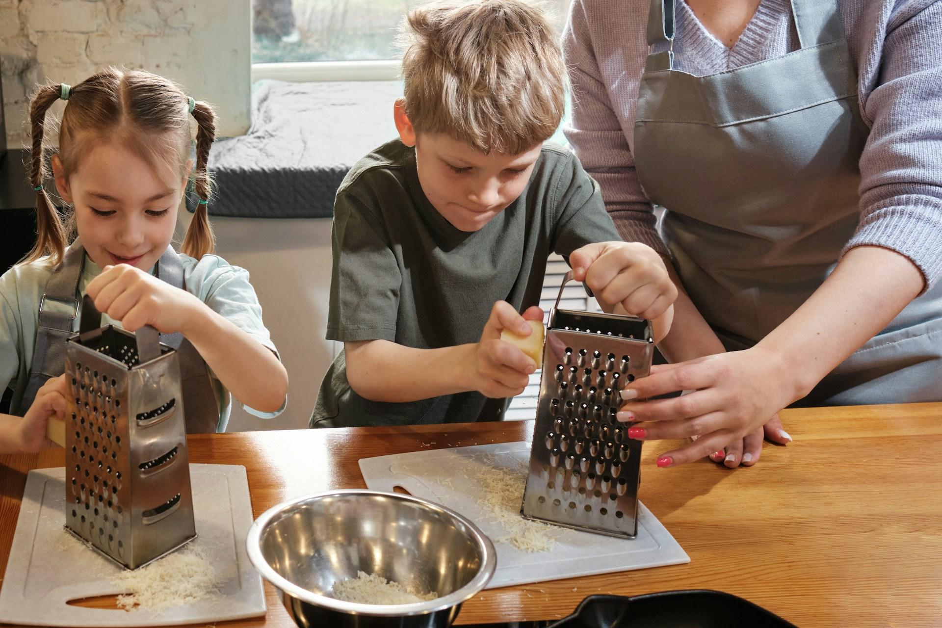 Two children use bell graters as an adult lends a hand.