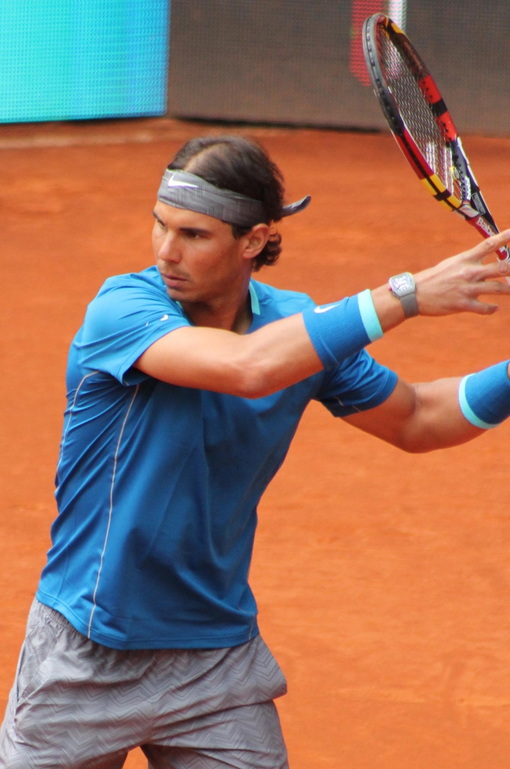 A male tennis player on a clay court prepares to return the ball. 