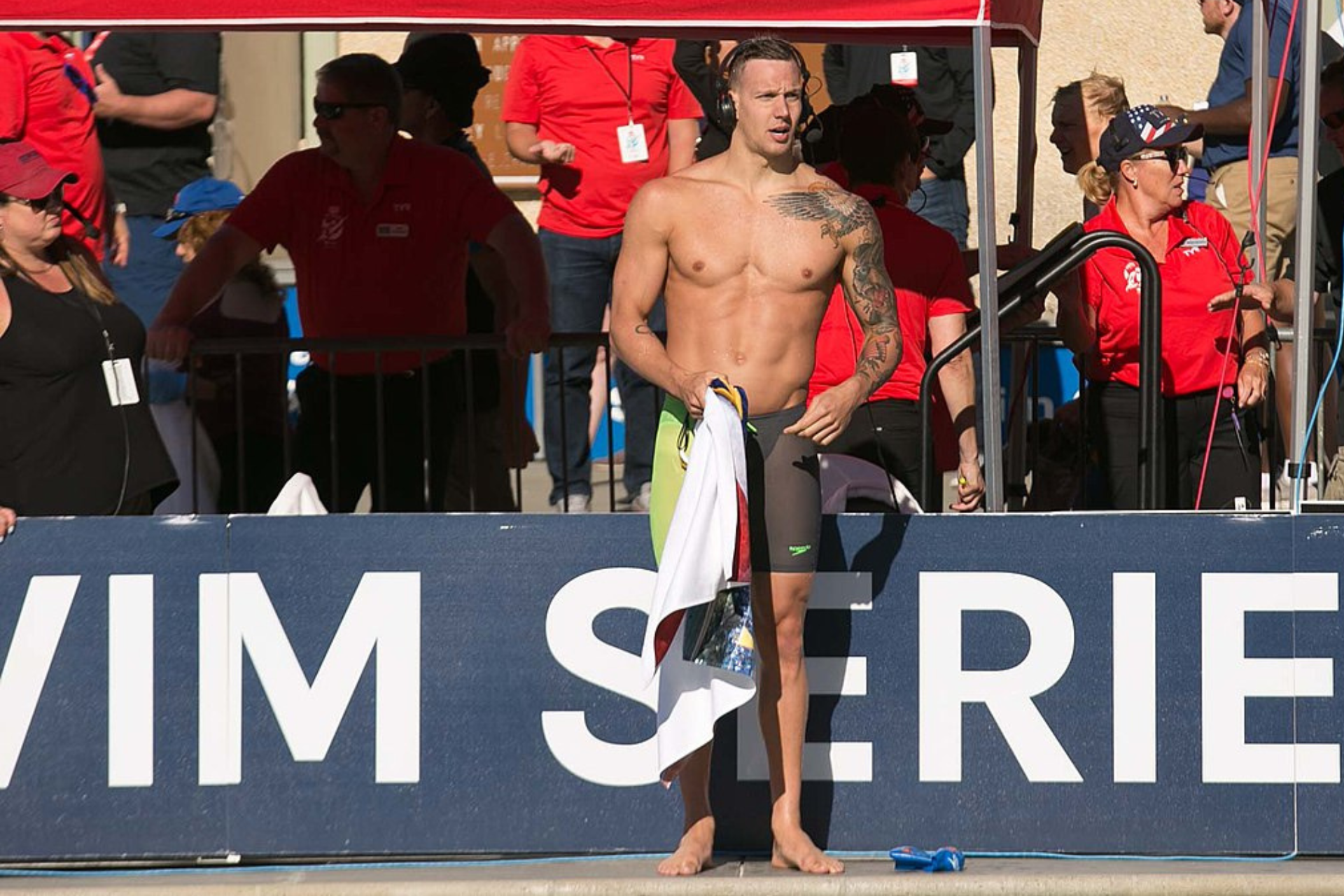 Caeleb Dressel stands confidently by the pool, hands on hips.