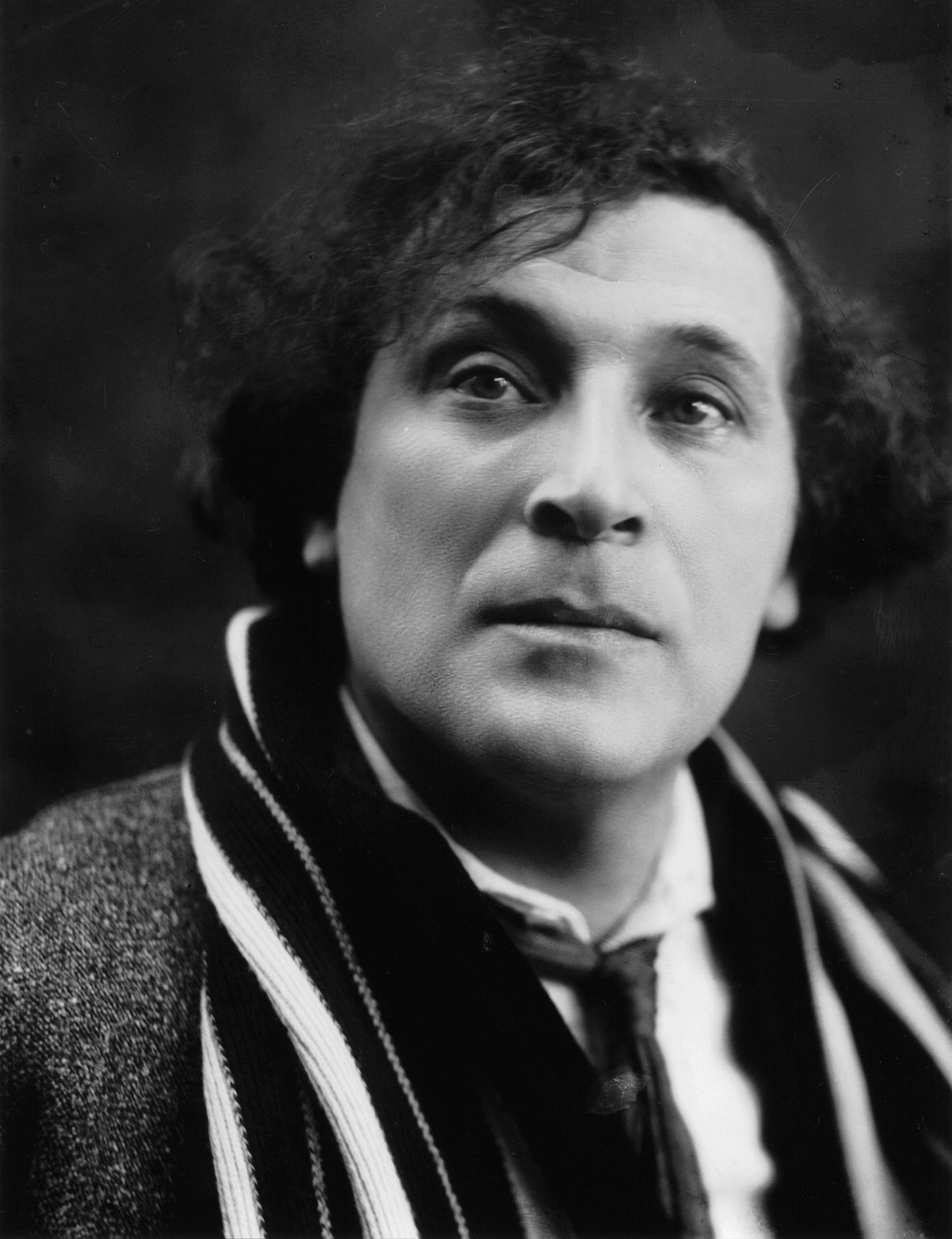 A greyscale image of a man wearing a suit with a scarf.