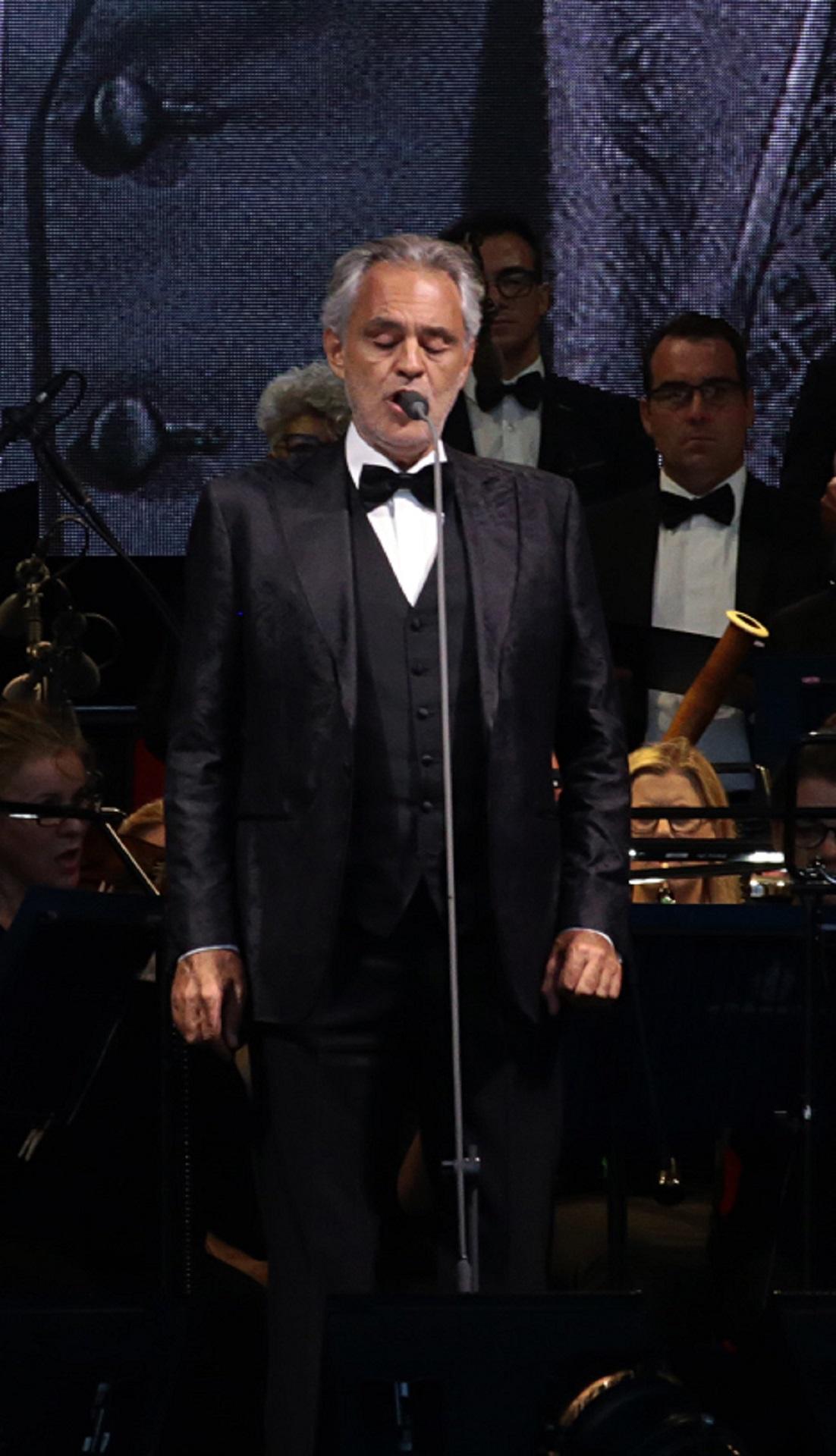 A man wearing a suit with bow tie sings in front of an orchestra.